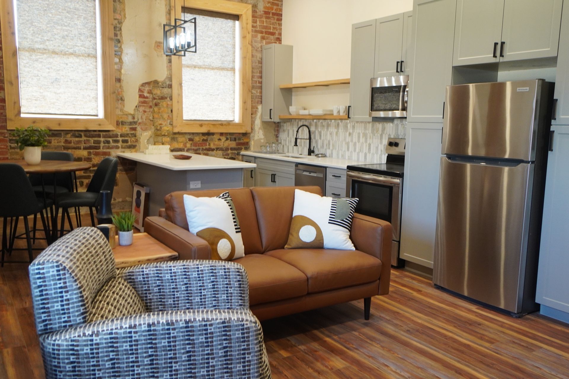Modern open-concept living space with a kitchen, dining area, and living room with Exposed brick.