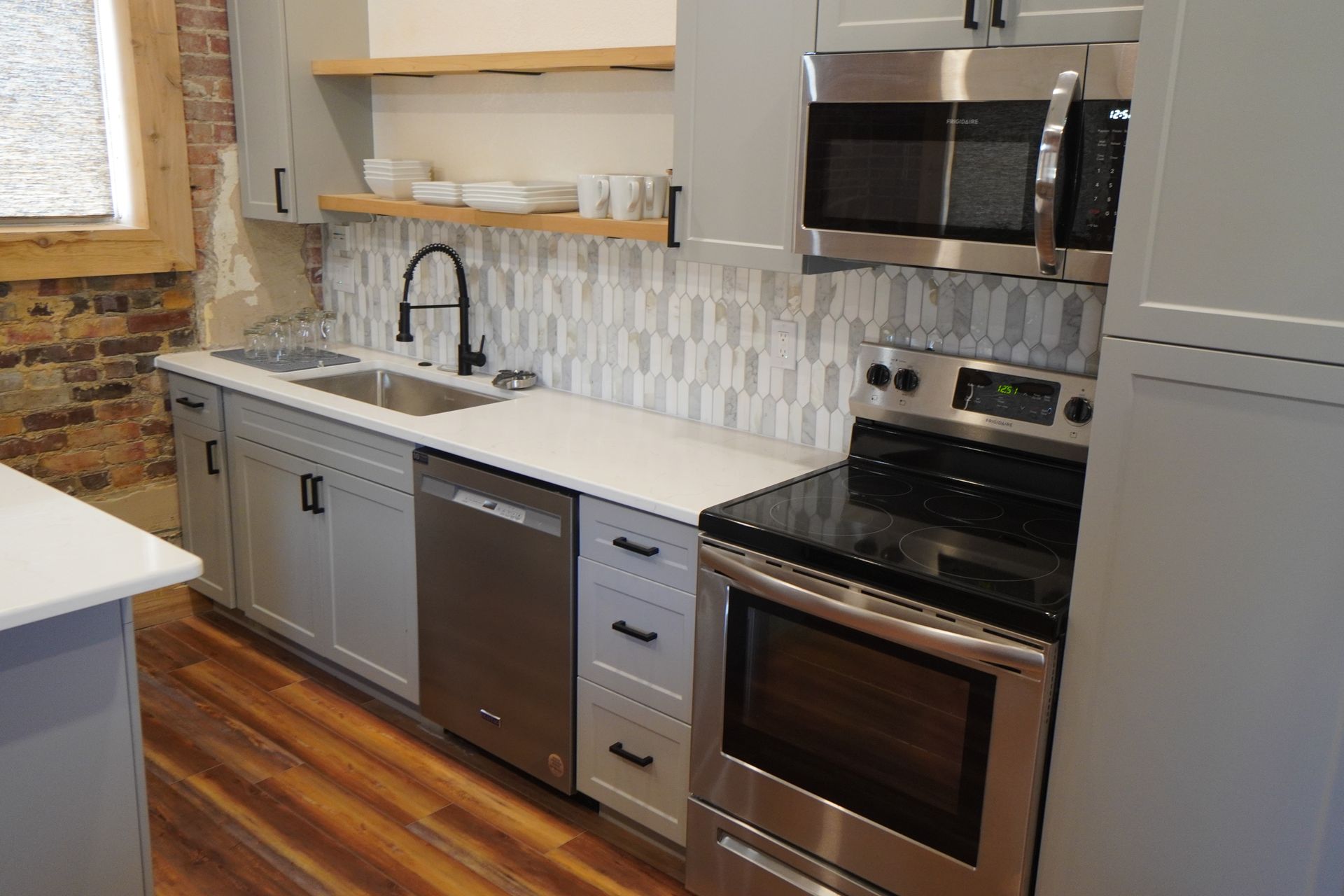 Modern kitchen with gray cabinets, stainless steel appliances, and white countertops.