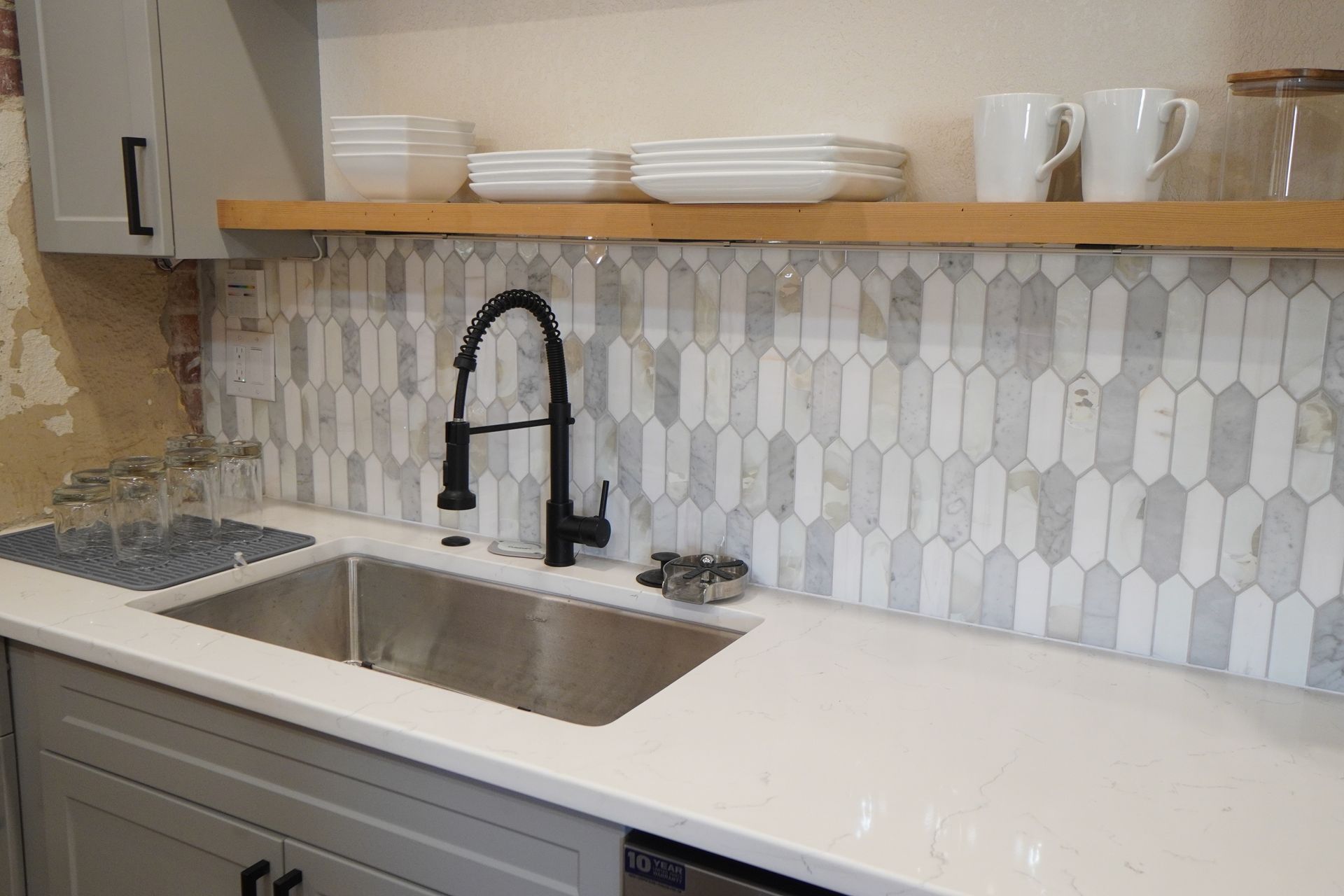 Kitchen sink with a black faucet, white countertops, and decorative backsplash tile.
