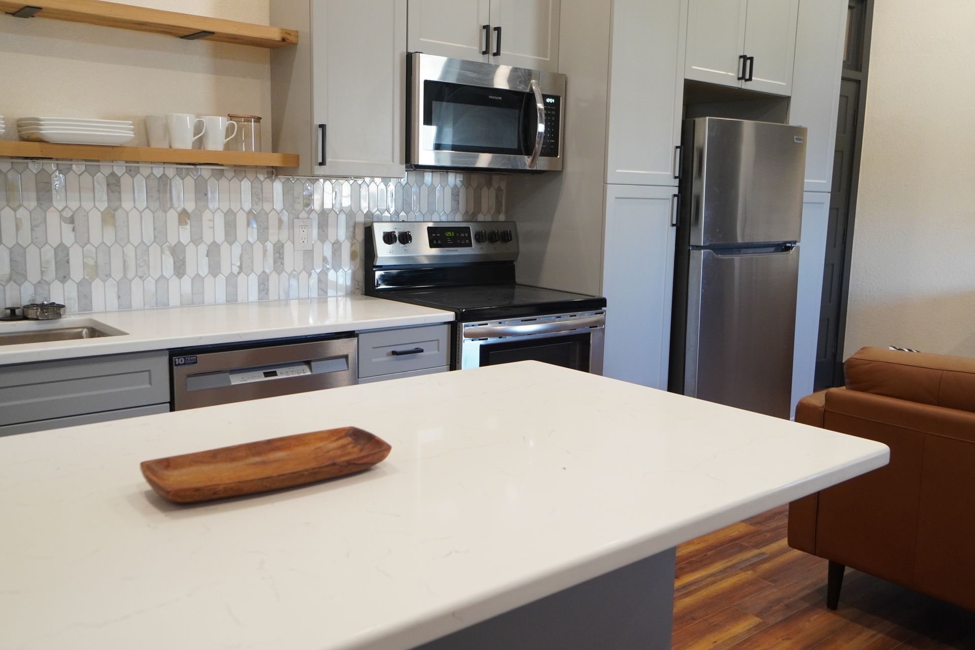 Modern kitchen with grey cabinets, stainless steel appliances, and a white countertop island.