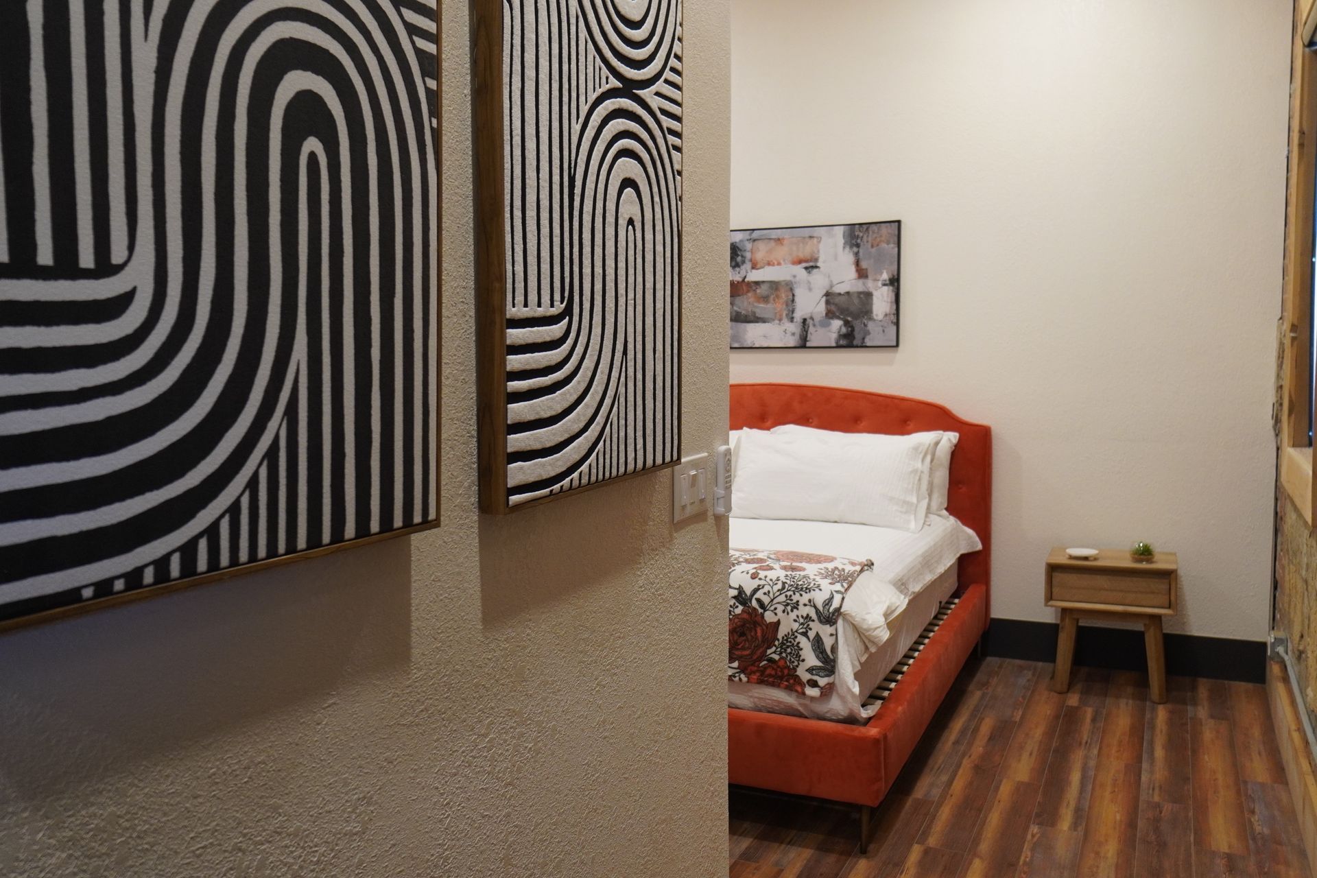Bedroom with orange bed, abstract art, and wooden nightstand.