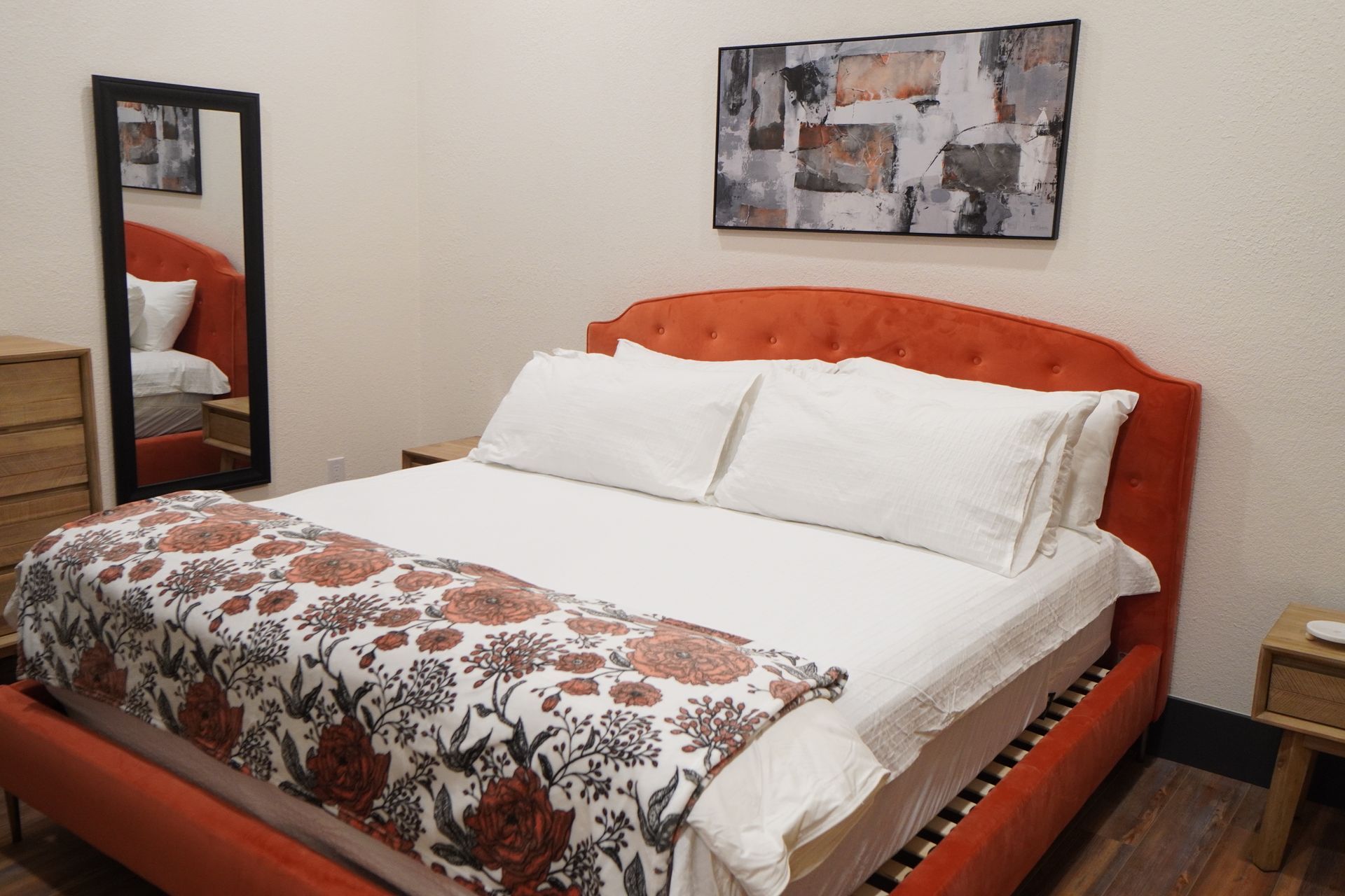 Bedroom with orange upholstered bed, white bedding, floral blanket, and abstract artwork.