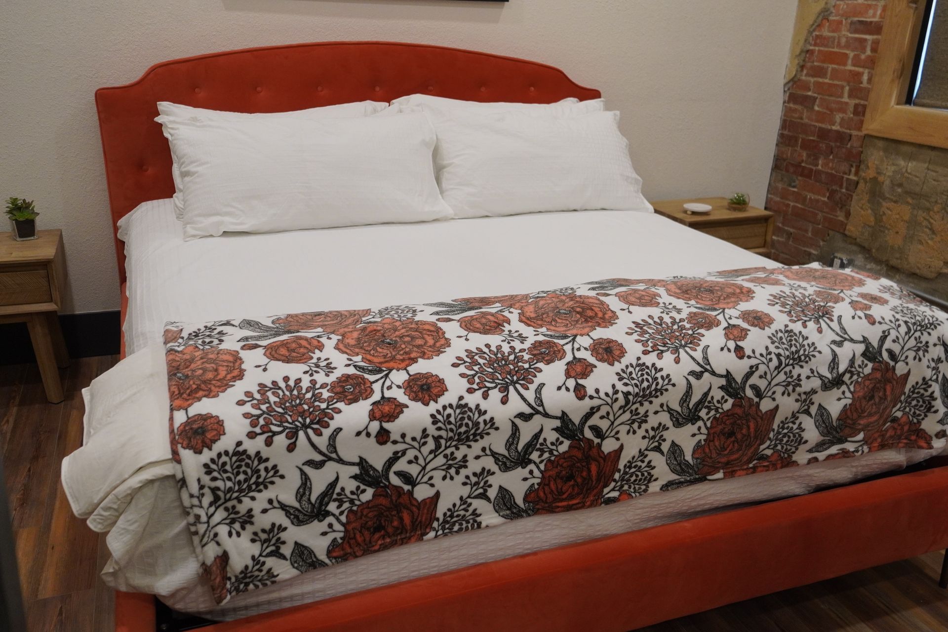 Orange bed with white bedding, floral blanket, and two pillows. Side tables with plants on each side.