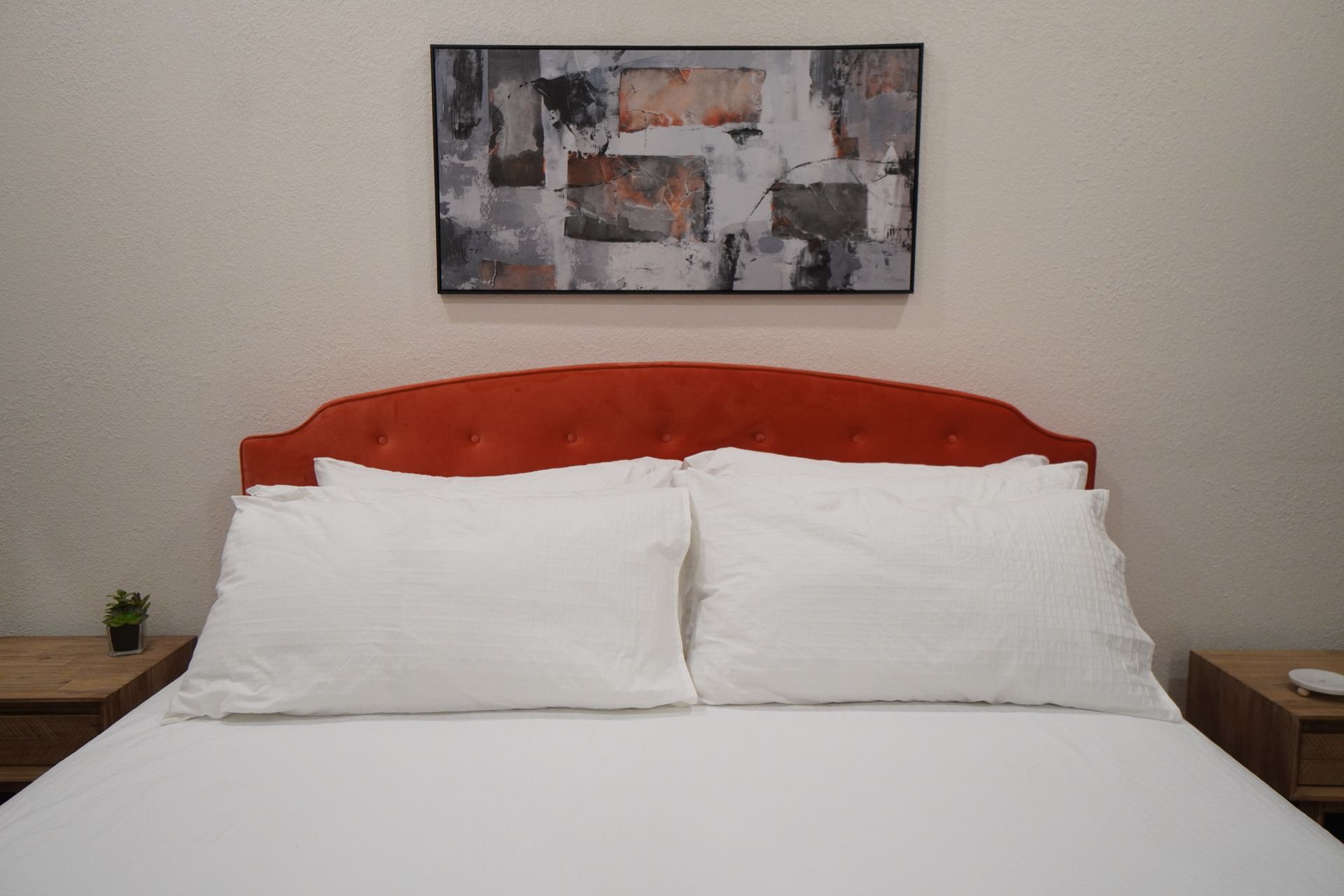 Bed with orange headboard, white bedding, two pillows, artwork above.