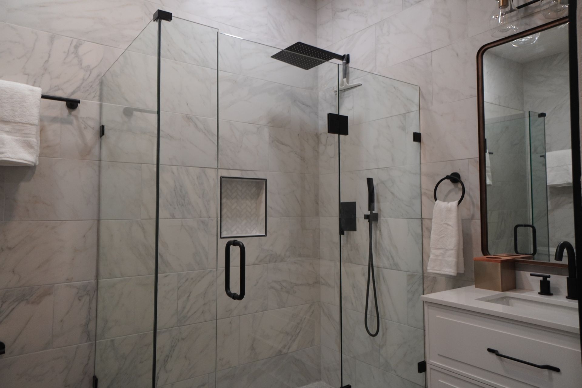 Modern bathroom with marble tile, glass shower, black fixtures, and a white vanity.