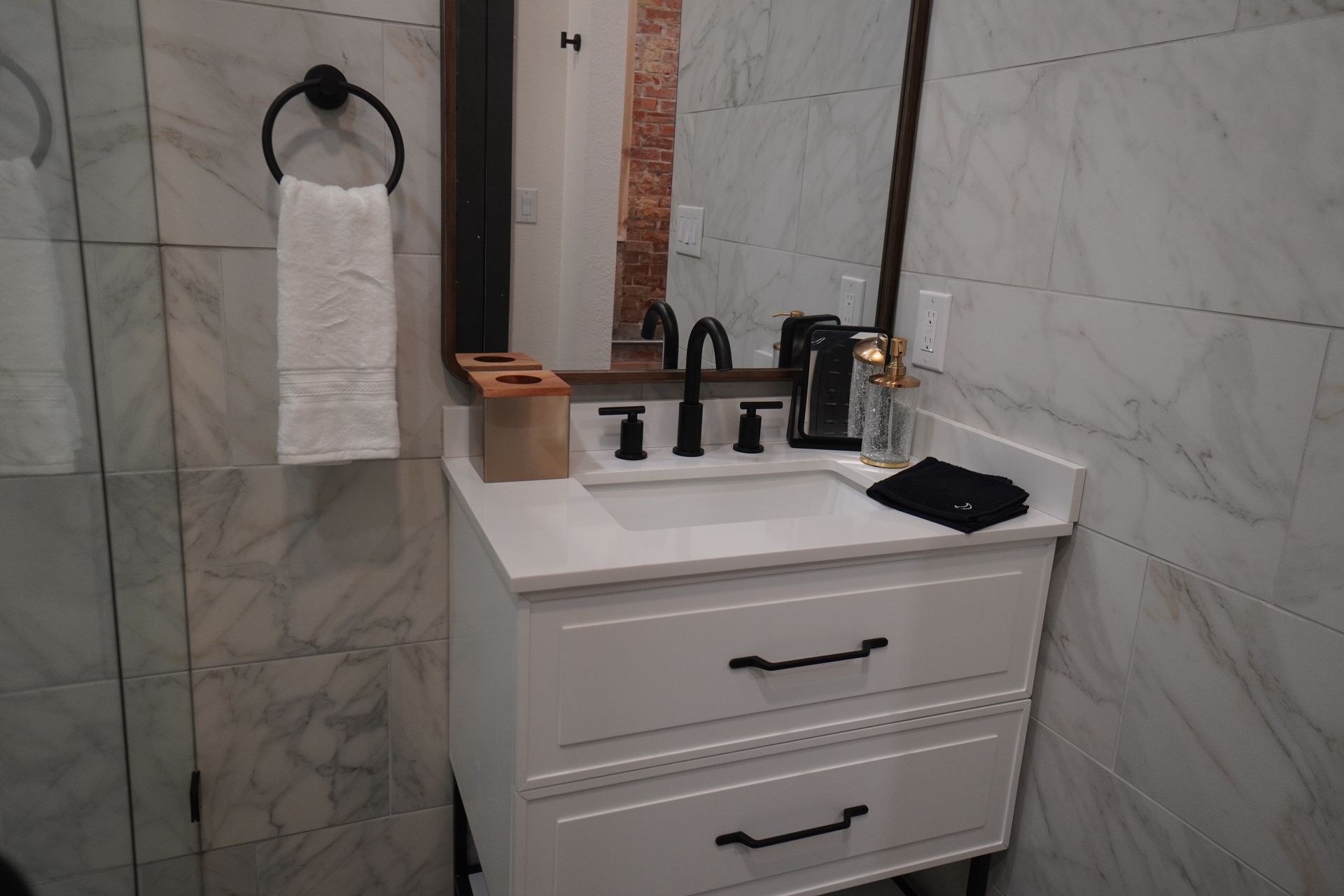 Bathroom with white vanity, black fixtures, and marble-look tile. 