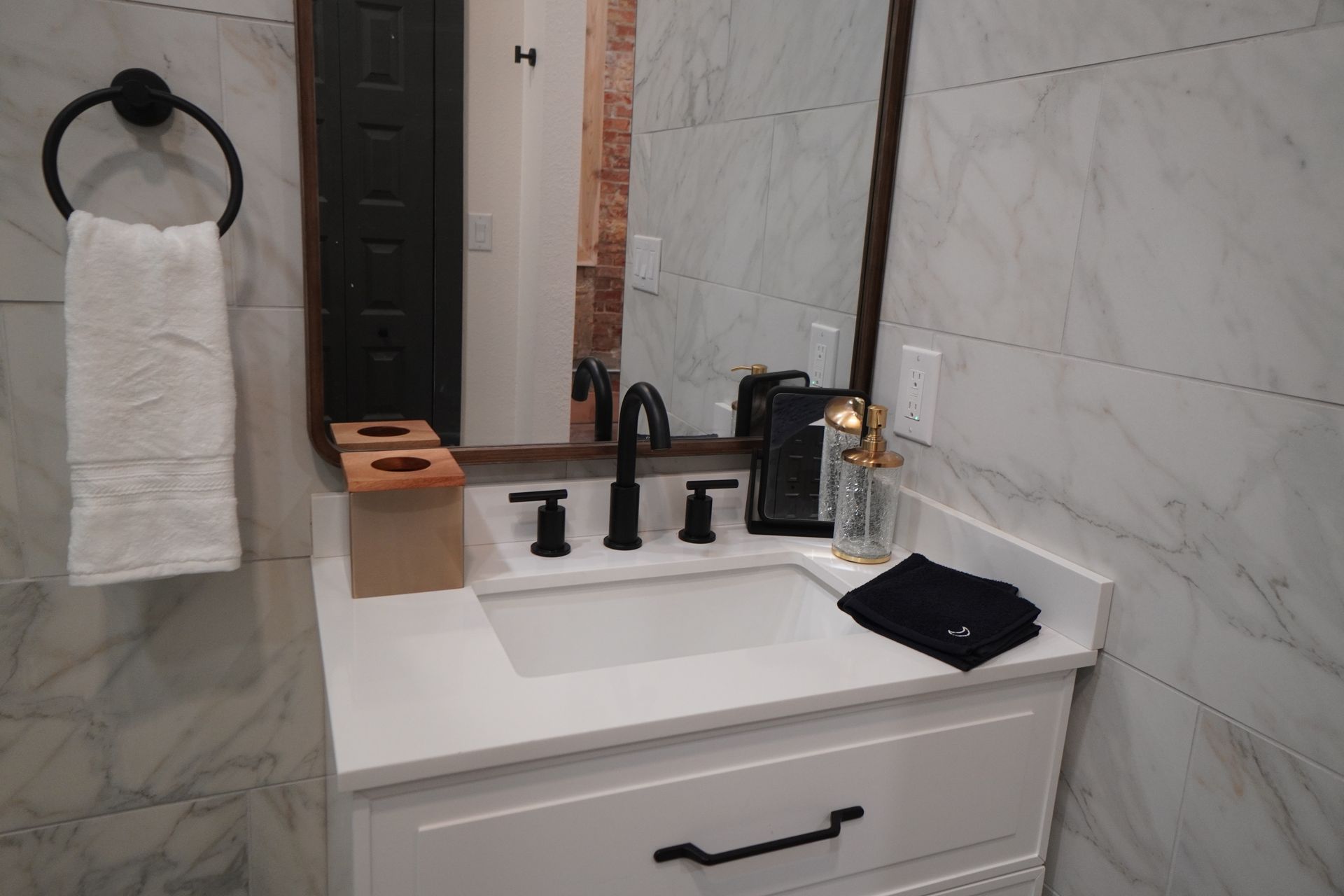 Bathroom vanity with white countertop, black fixtures, and white marble tile.