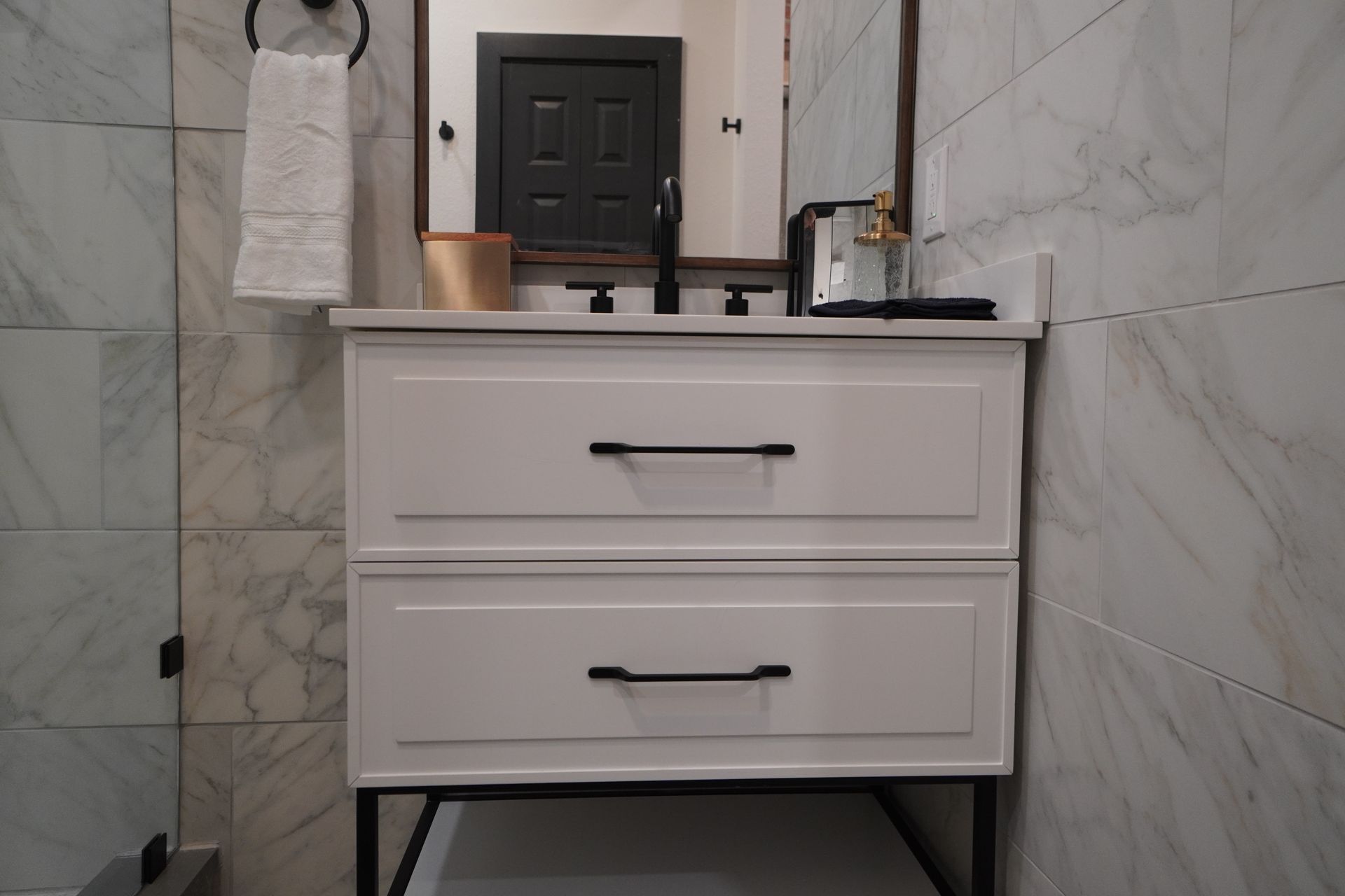 White bathroom vanity with black hardware and a mirror.