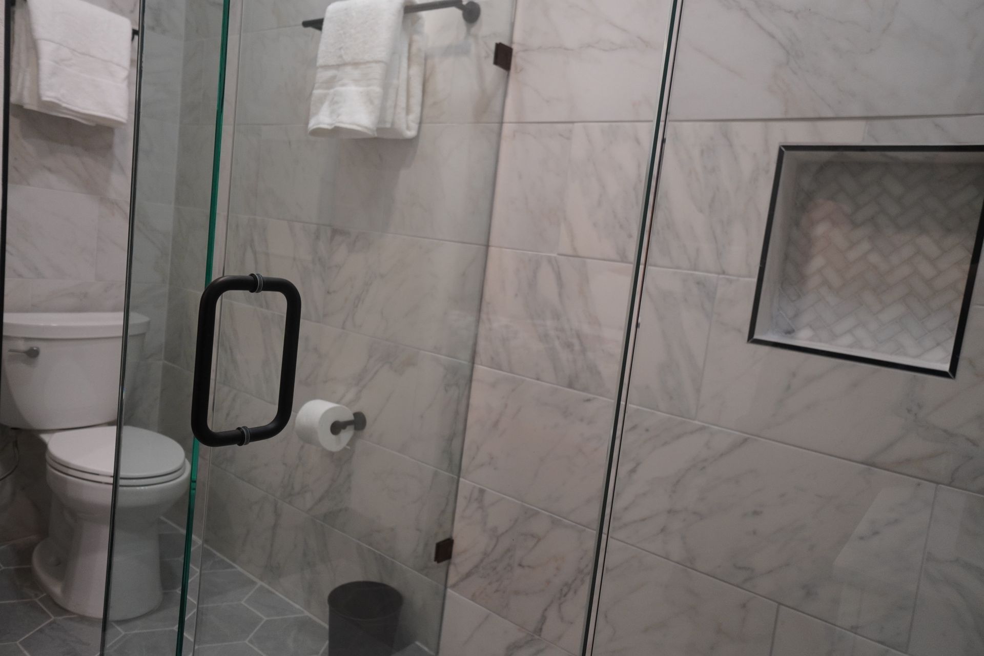 Bathroom with a glass shower door, a toilet, and light-colored tiled walls.