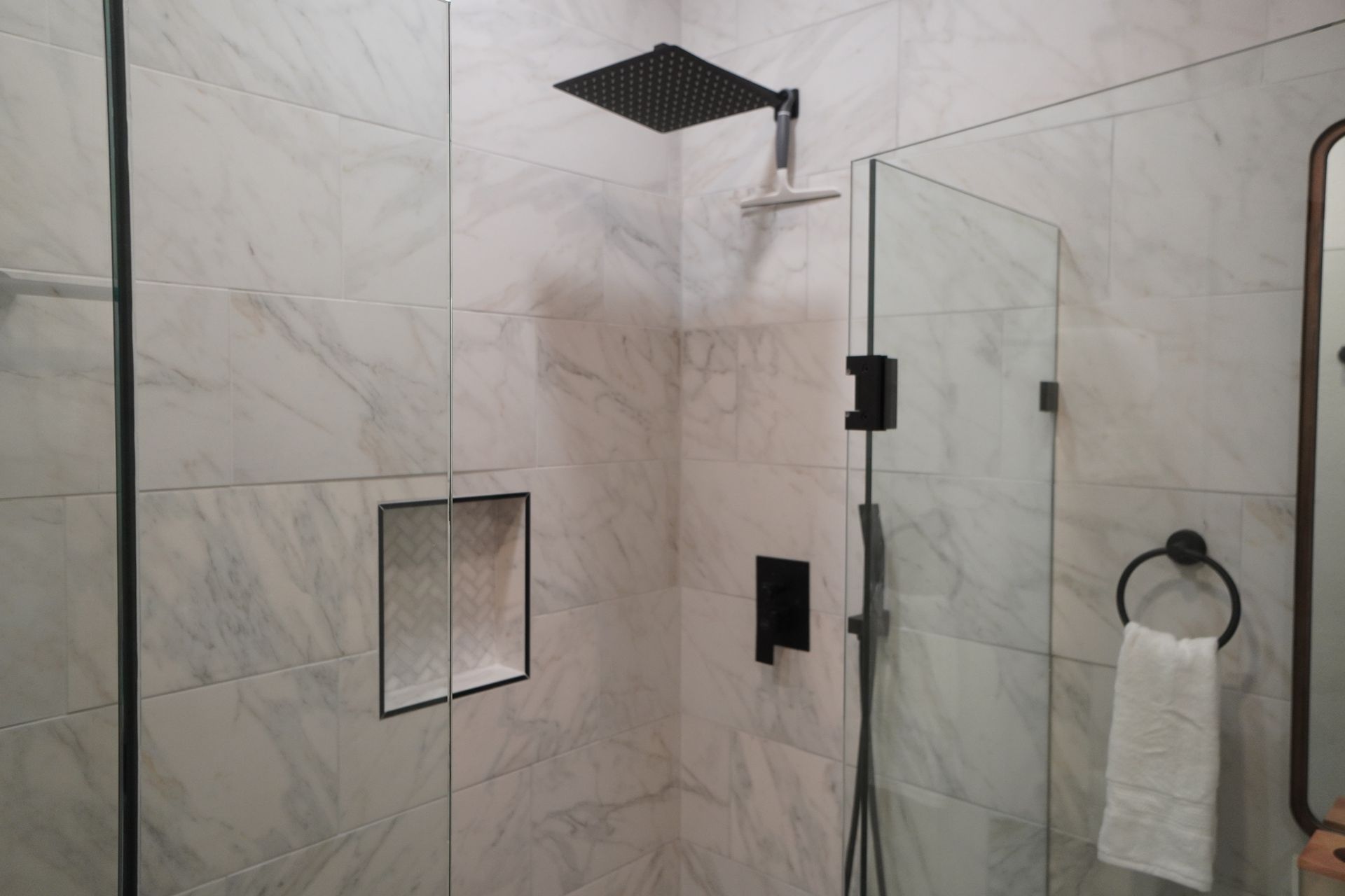 Modern bathroom with white marble tile, black shower fixtures, and glass shower door.