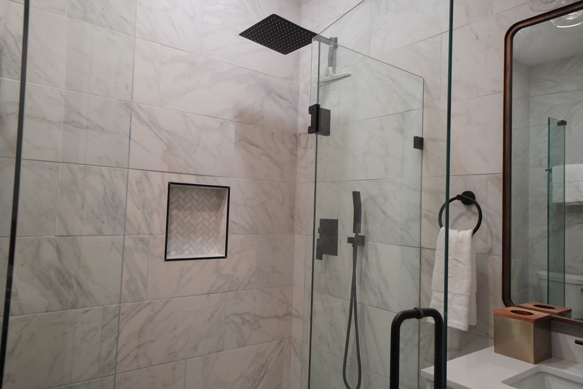 Modern bathroom with glass shower door, black fixtures, and marble tile walls.