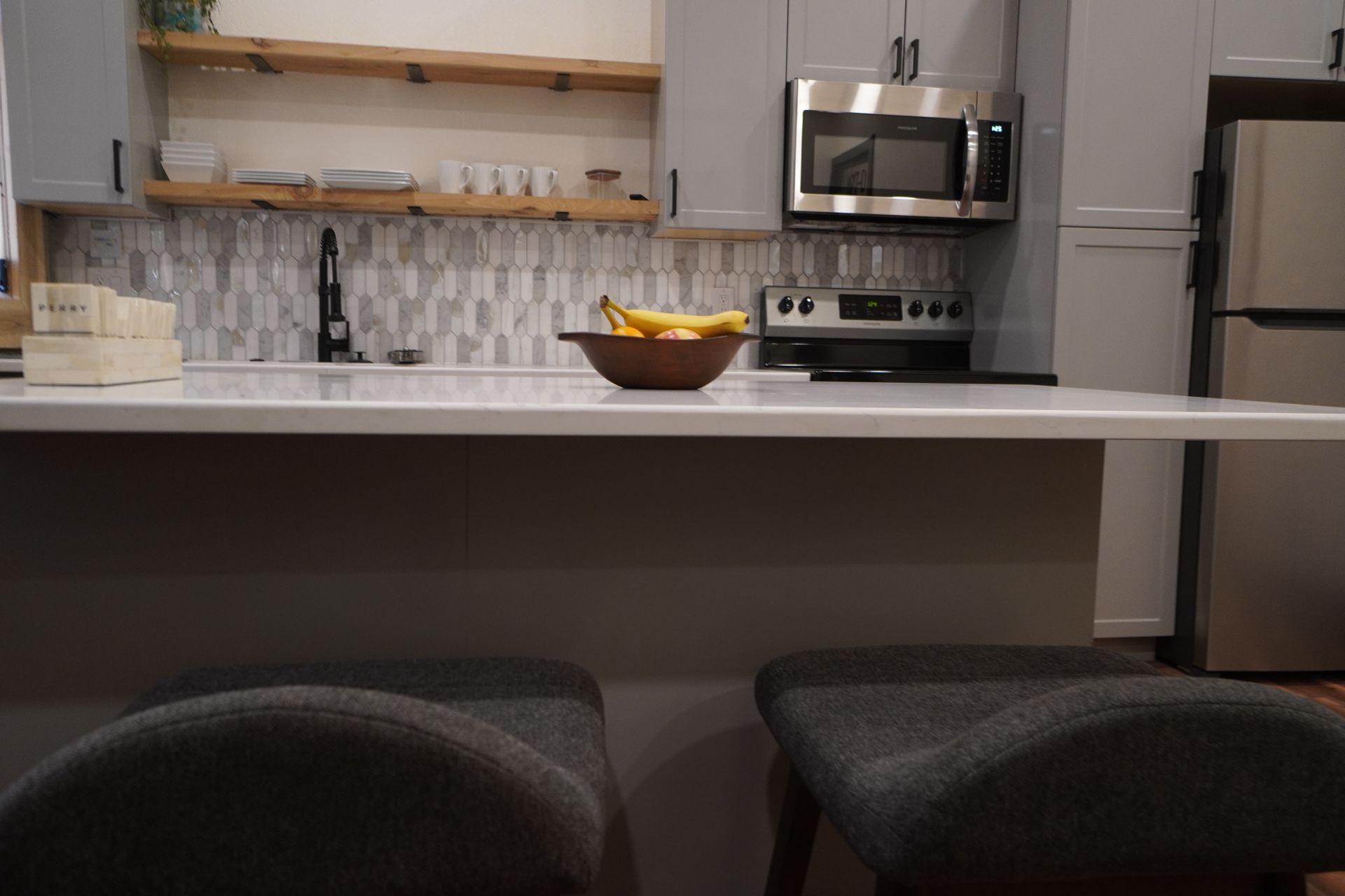 Kitchen with white counter, stools, and appliances. Bananas sit in a bowl on the counter.