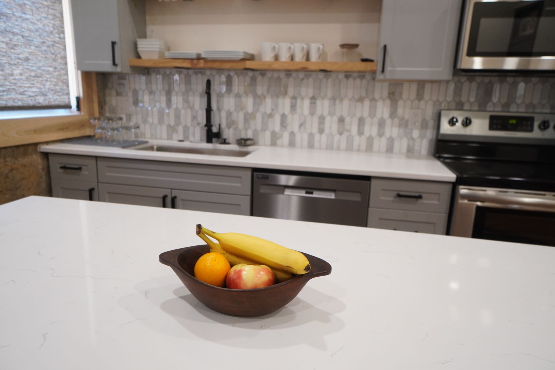 Kitchen with a fruit bowl on a white countertop; gray cabinets, stainless steel appliances, and tile backsplash.