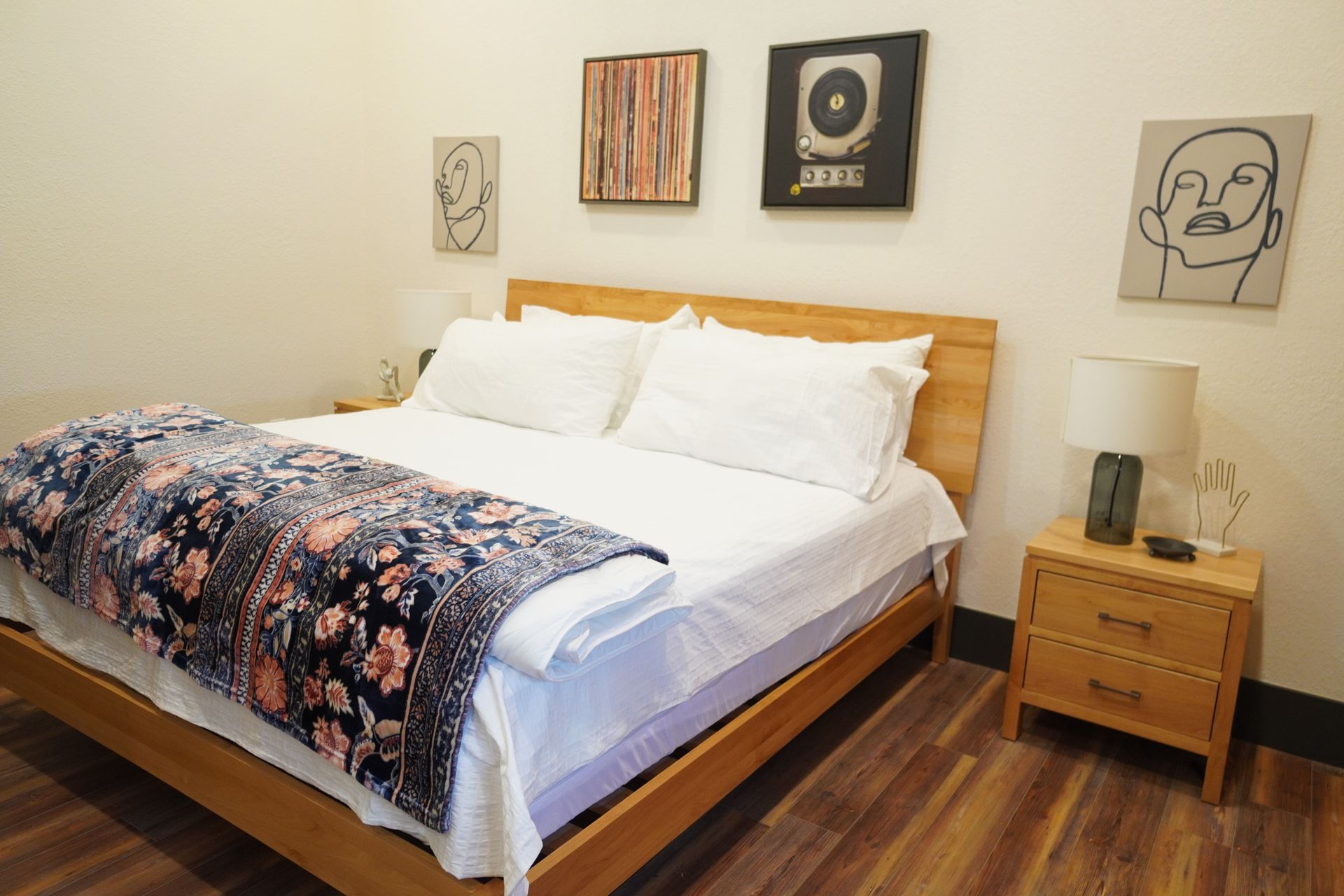 Bedroom with wooden bed, nightstand, art prints, and floral blanket.