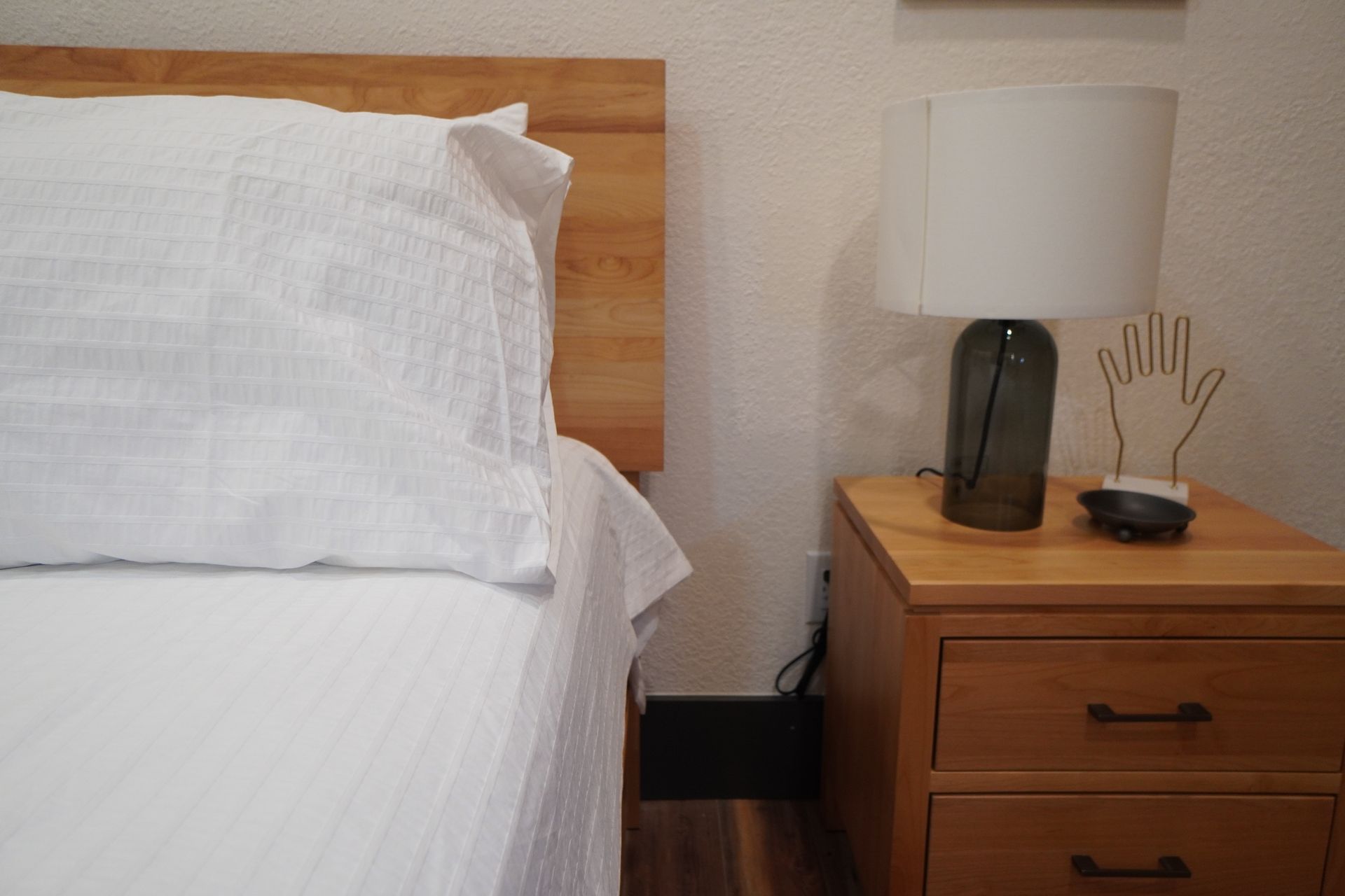 Bed with white linens, wooden headboard, bedside table with lamp, and decorative hand sculpture.