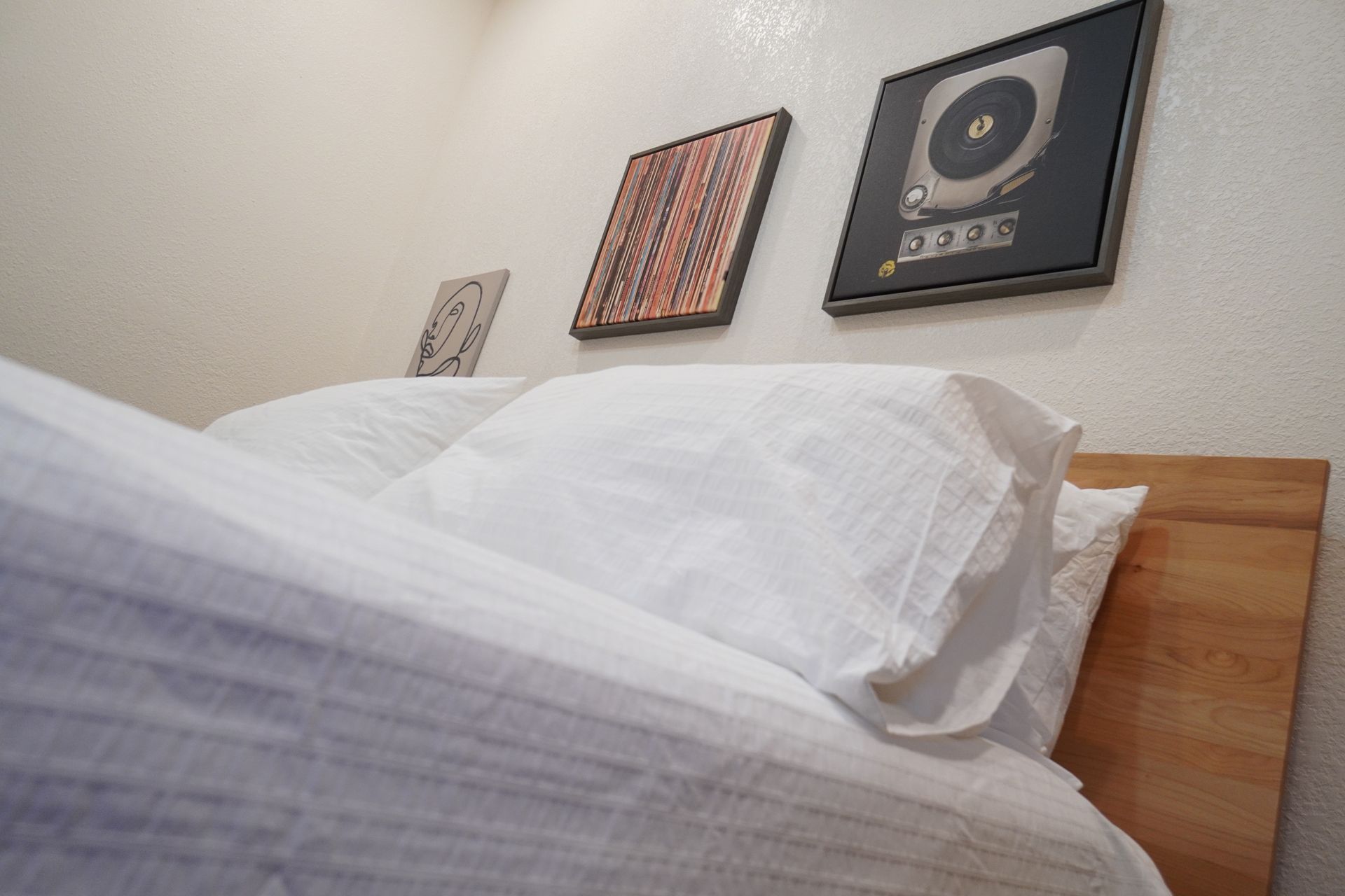 Bed with white linens and pillows, wooden headboard, artwork on the wall.