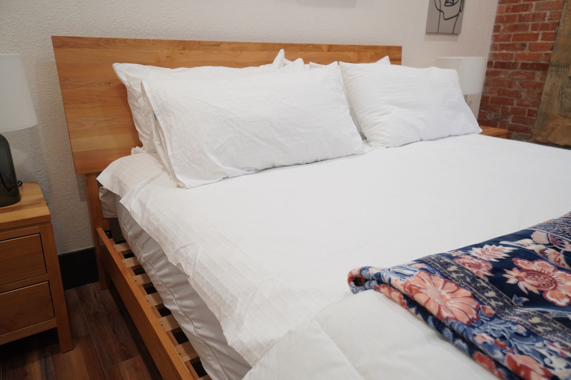 Bed with white linens, wooden frame and headboard. A patterned blanket is draped on the foot.