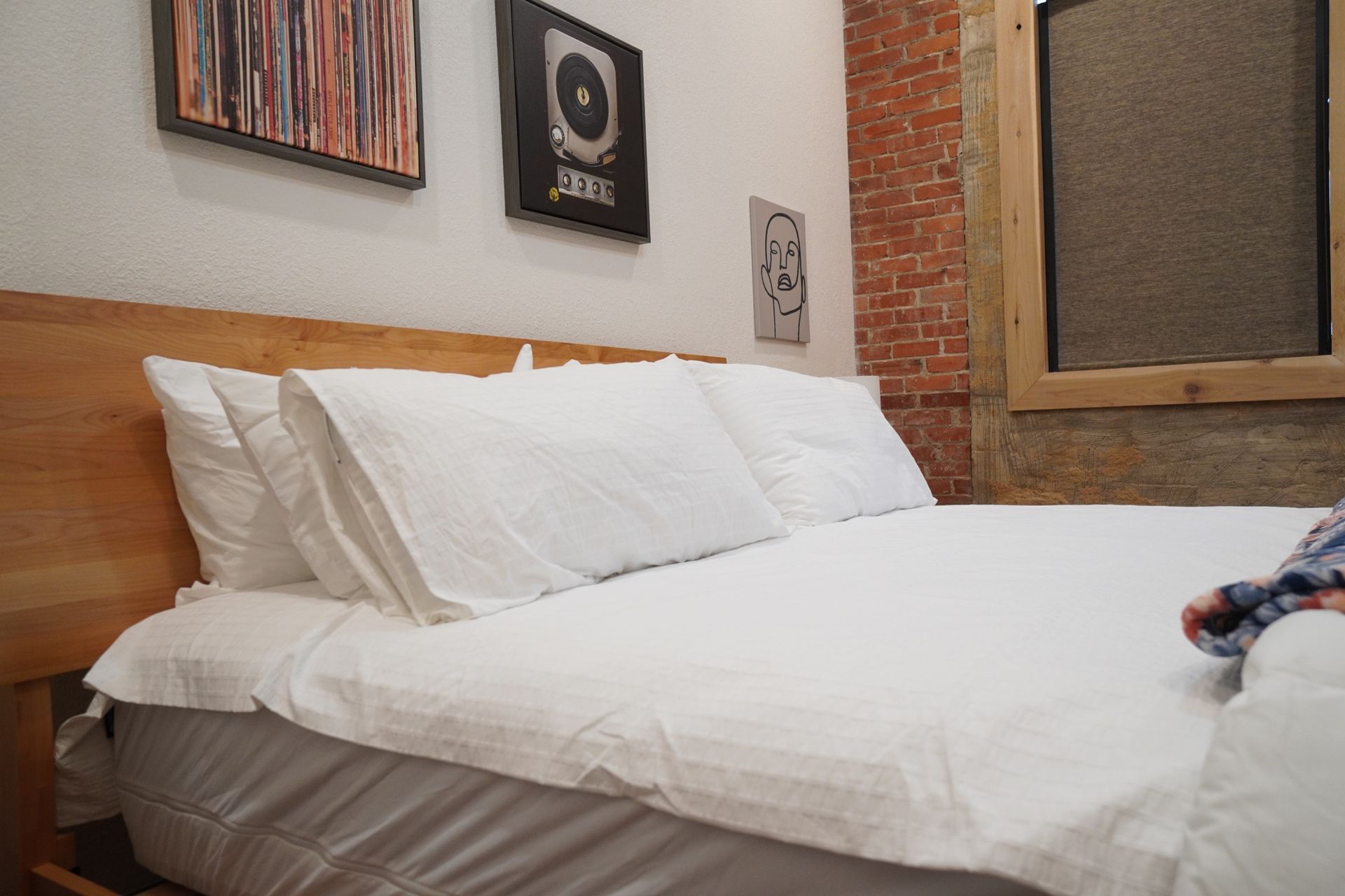 Bedroom with a bed made with white linens, wooden headboard, brick wall, and framed artwork.