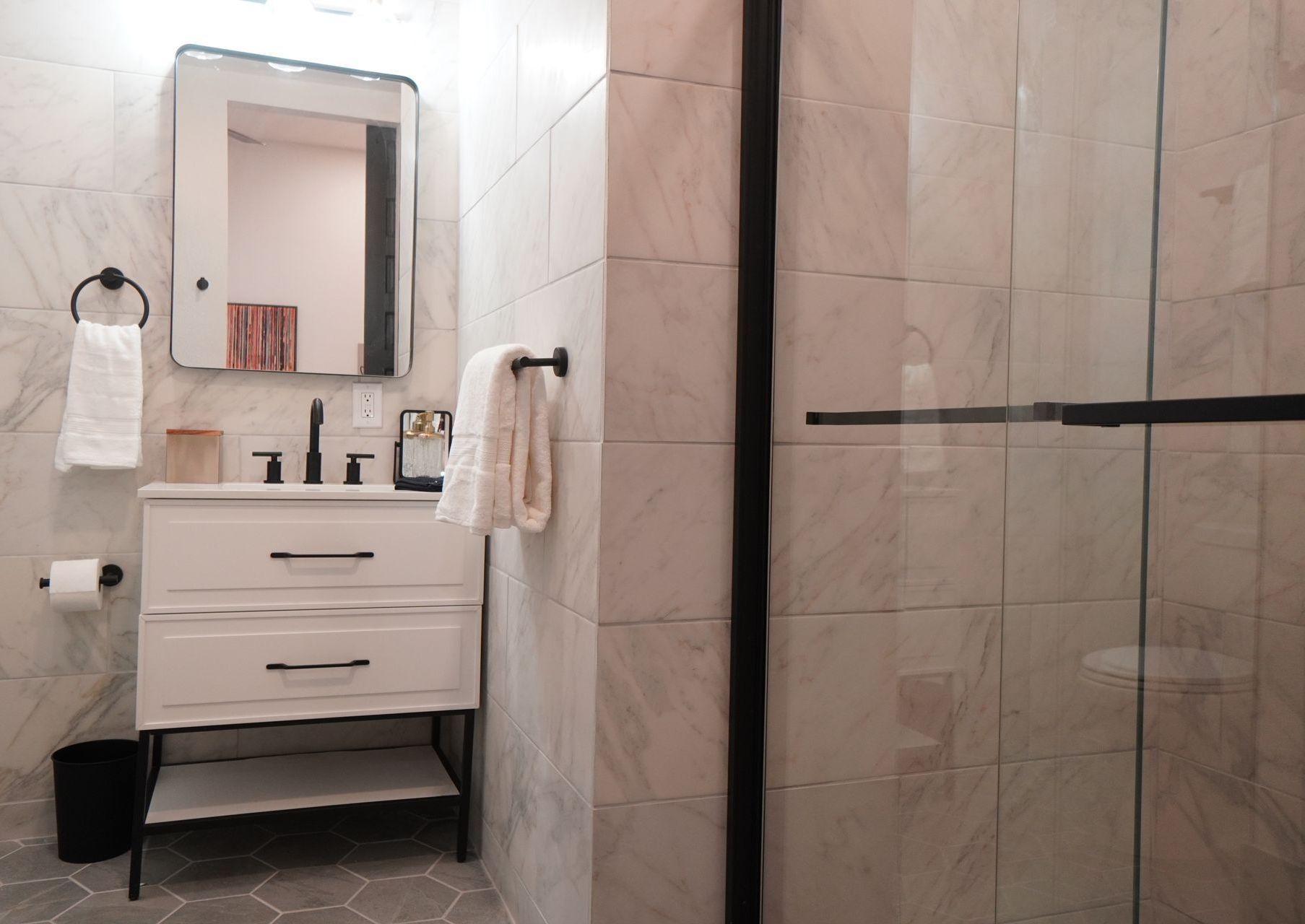 White bathroom with black accents, vanity, shower with glass door, and tiled walls.