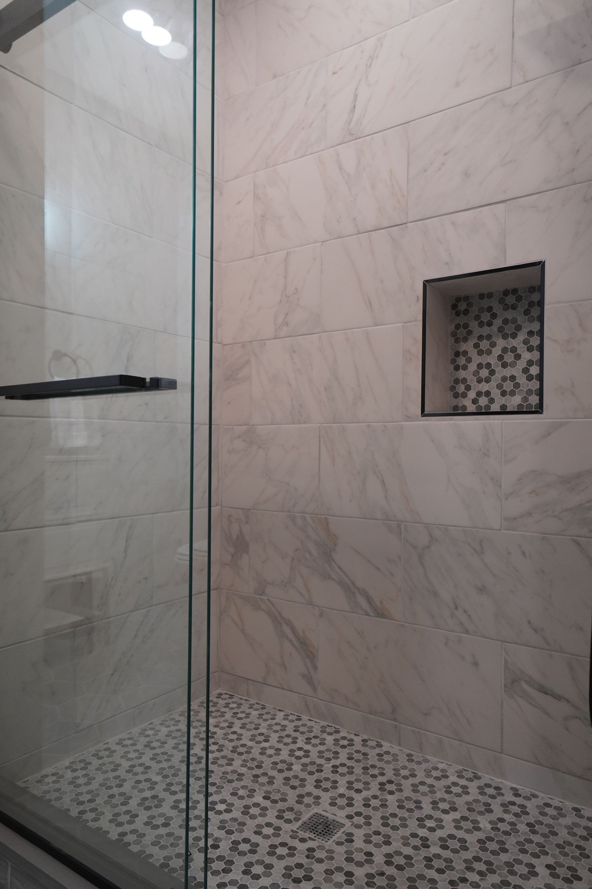 Shower with marble-like wall tile and a patterned floor tile. A built-in shelf has a contrasting patterned tile.