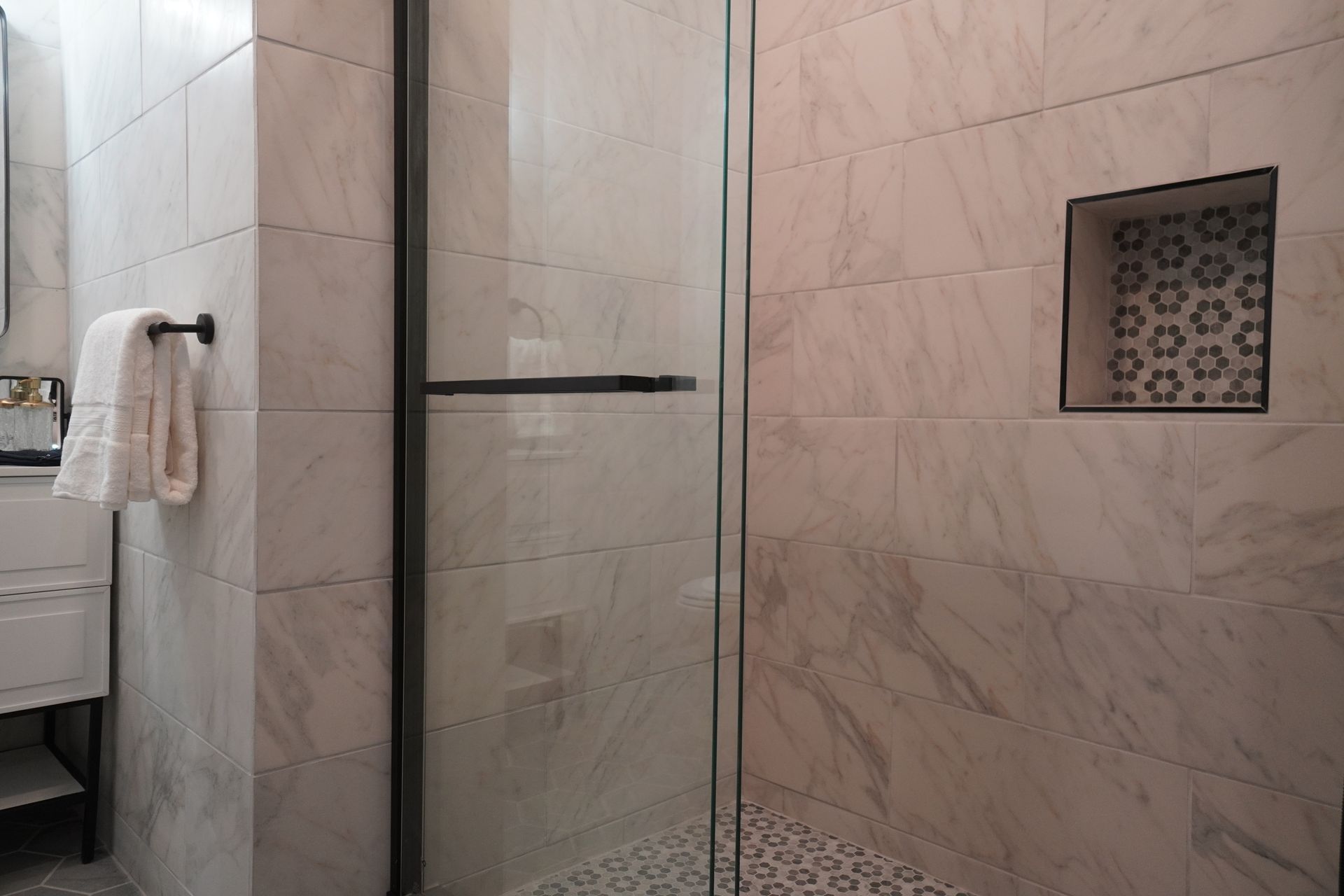 Modern bathroom with a glass shower, white marble-look tile, and a decorative tile niche.