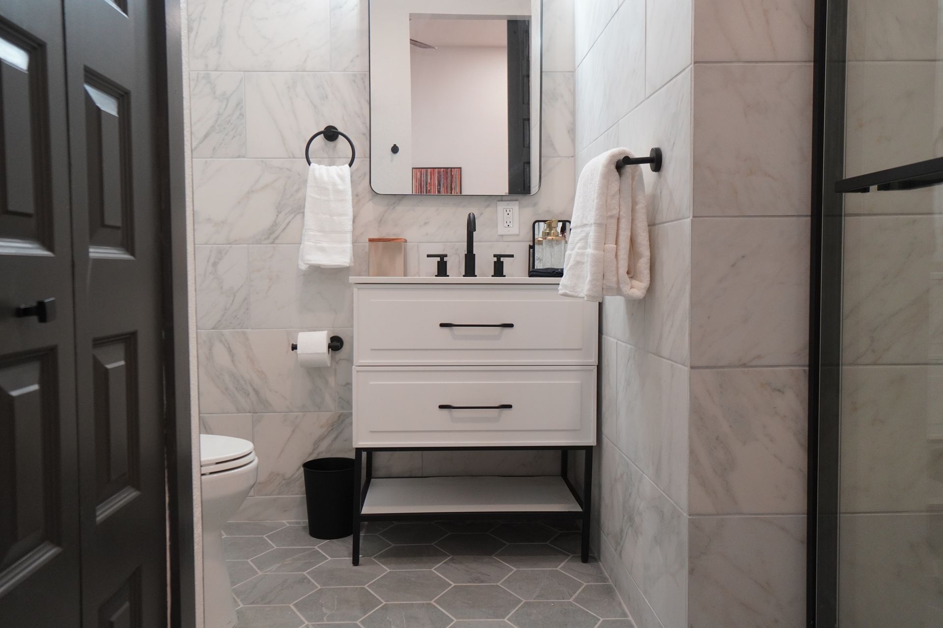 Bathroom with white vanity, black fixtures, gray tile, and a black door.