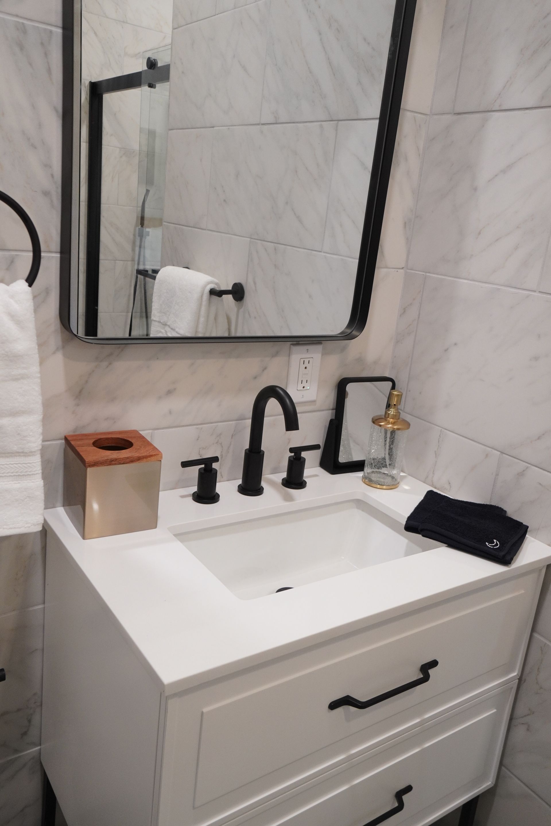 White bathroom vanity with black fixtures, mirror, and towel rack.