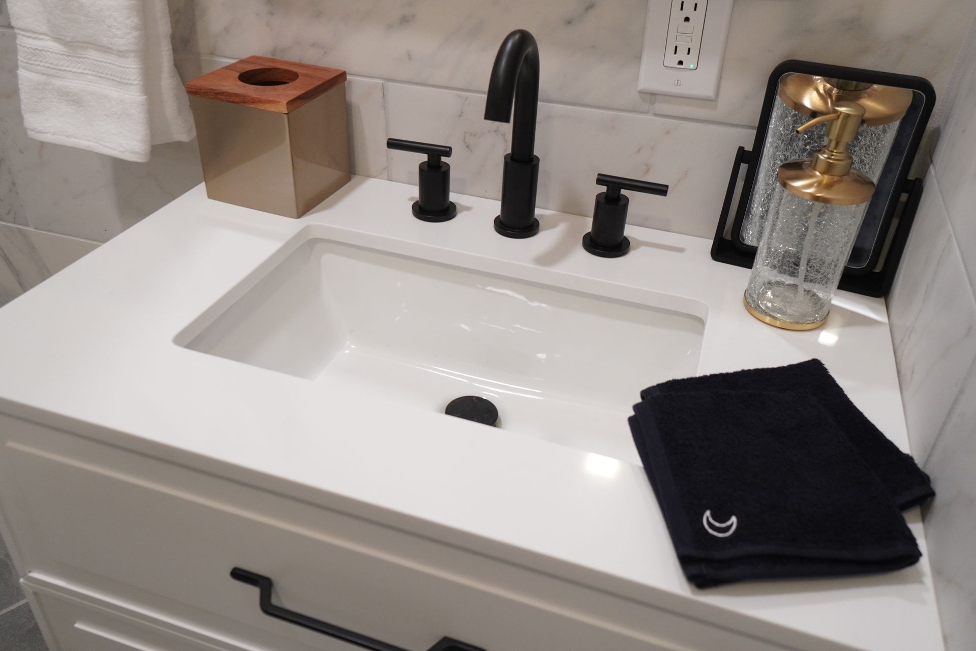 Bathroom sink with black fixtures and white countertop; black towel on the counter.