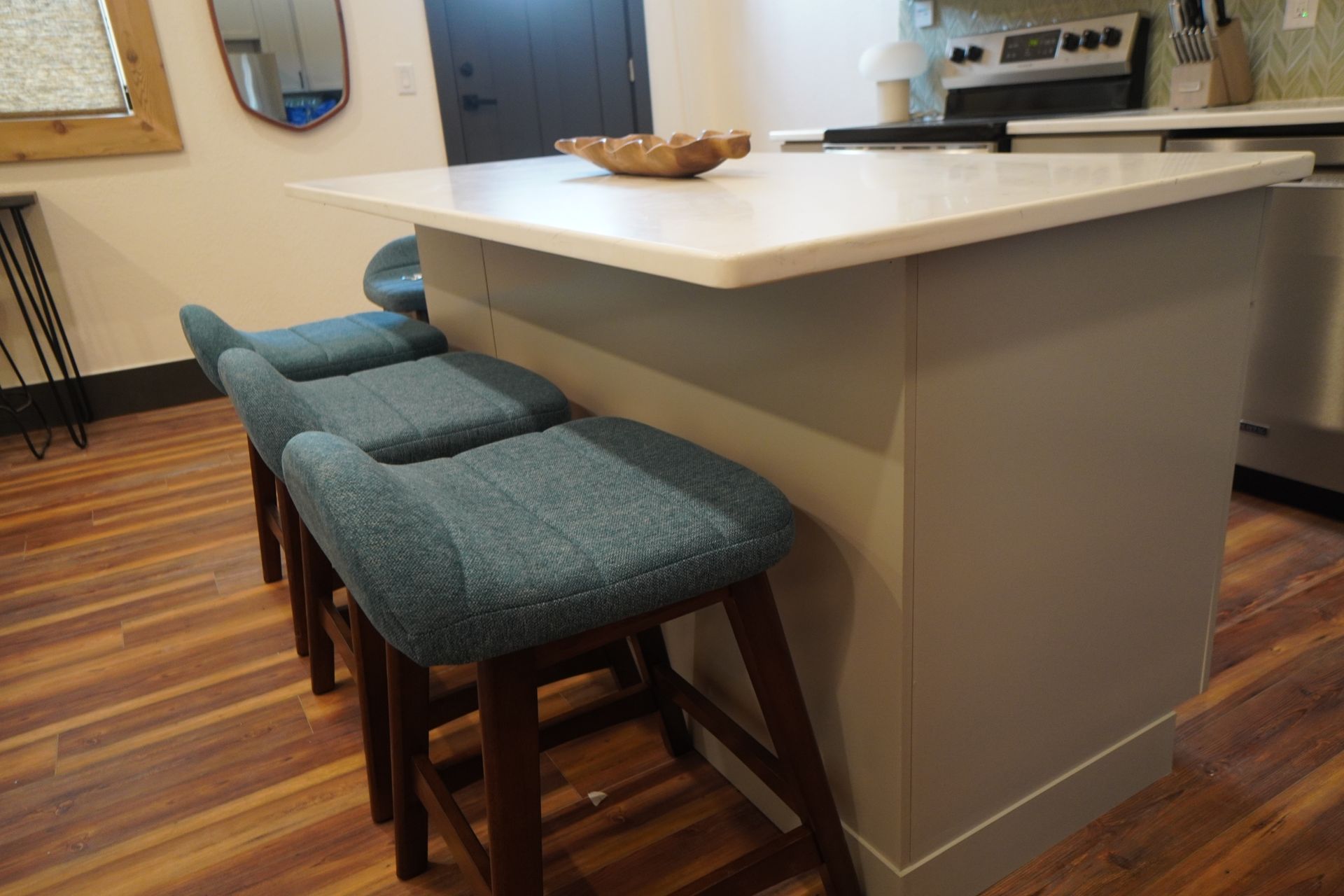 Kitchen island with three blue upholstered bar stools and a wooden bowl.
