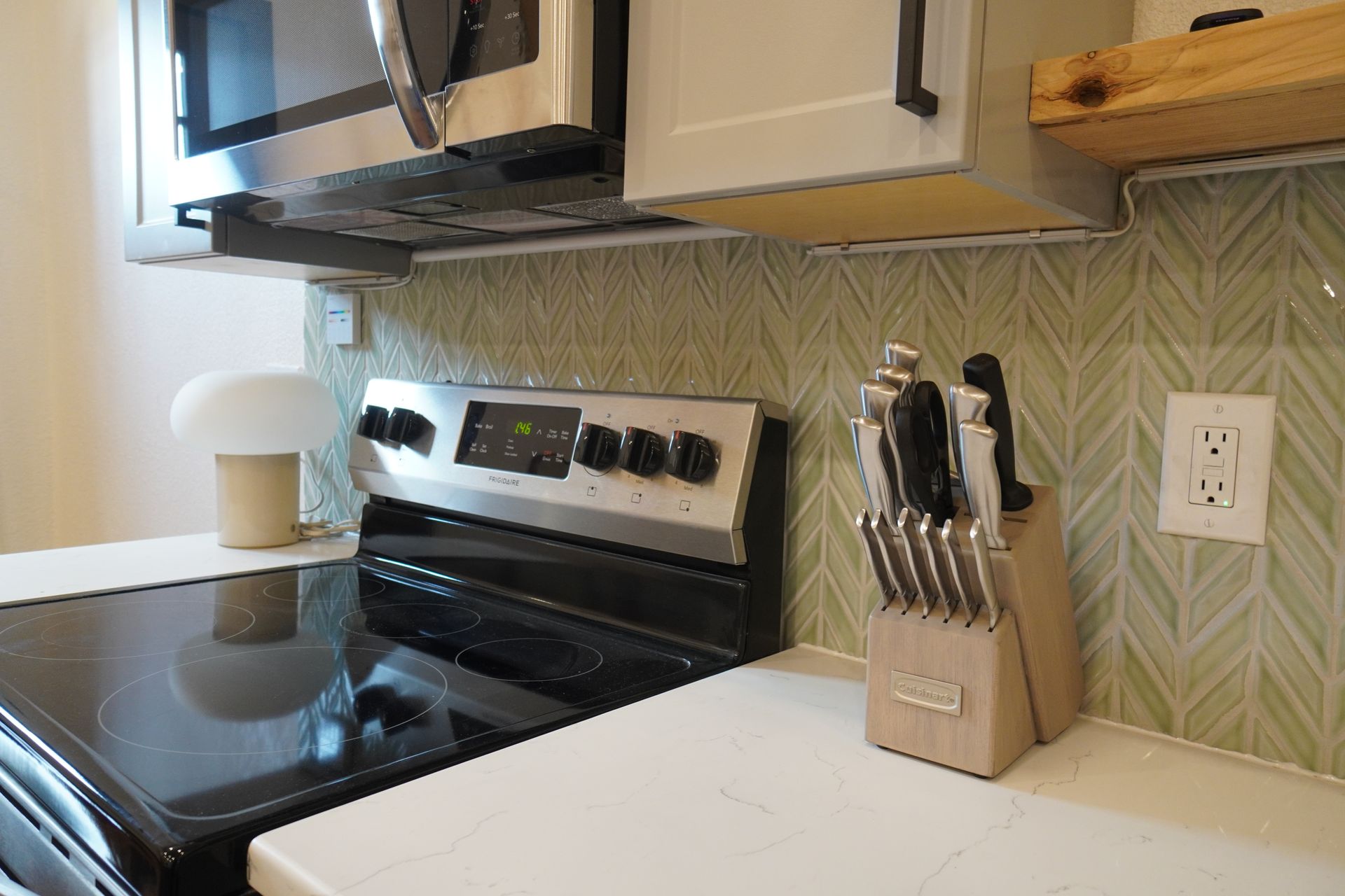 Kitchen stove with microwave above, counter with knife block and outlet.