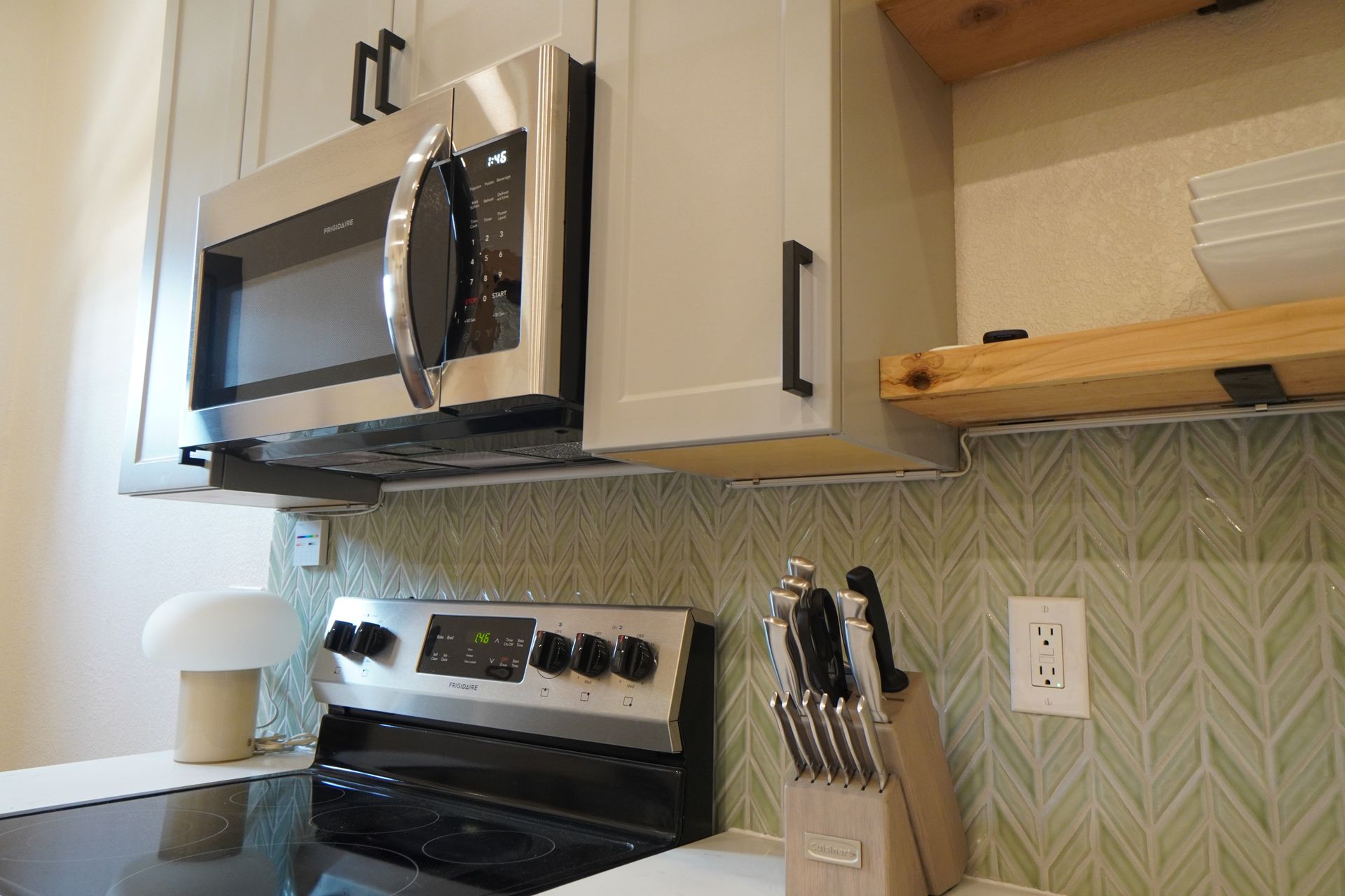 Kitchen with microwave above stove, cabinets, backsplash, and knife block.