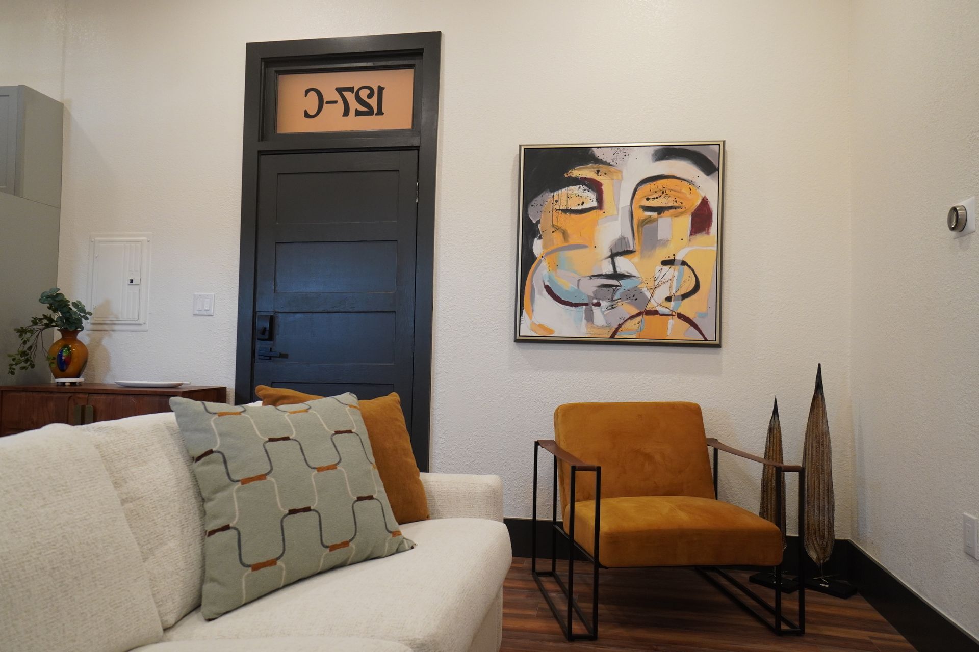 Cozy living room with artwork, mustard chair, white couch, and black door.