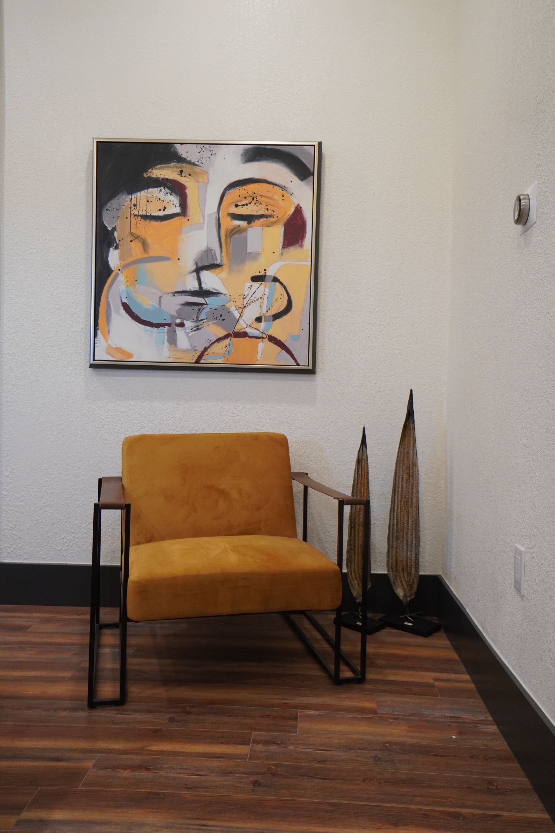 Modern art and yellow chair in a room with hardwood floors. Two wooden sculptures stand to the side.
