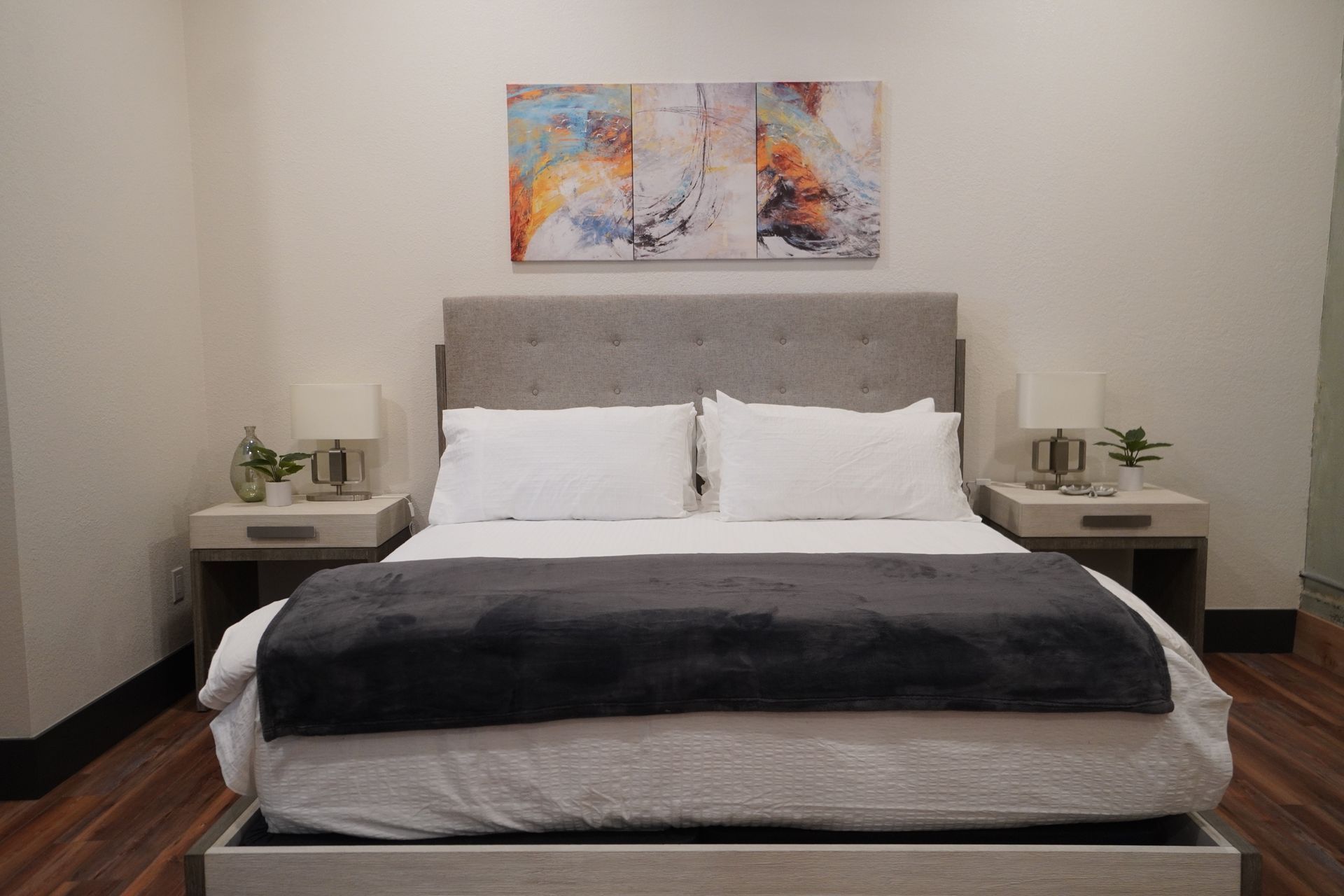 Bedroom with a gray upholstered headboard, white bedding, and abstract artwork.