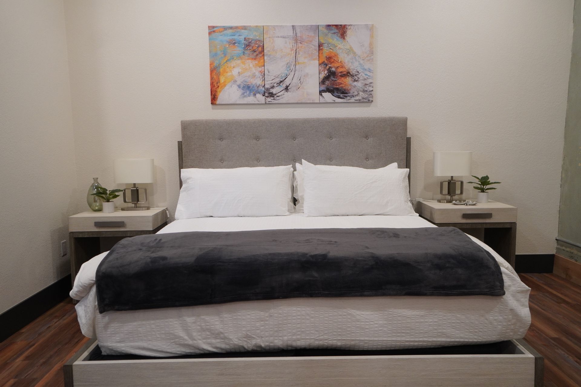 Bedroom with queen bed, gray headboard, white linens, two nightstands, artwork above the bed.