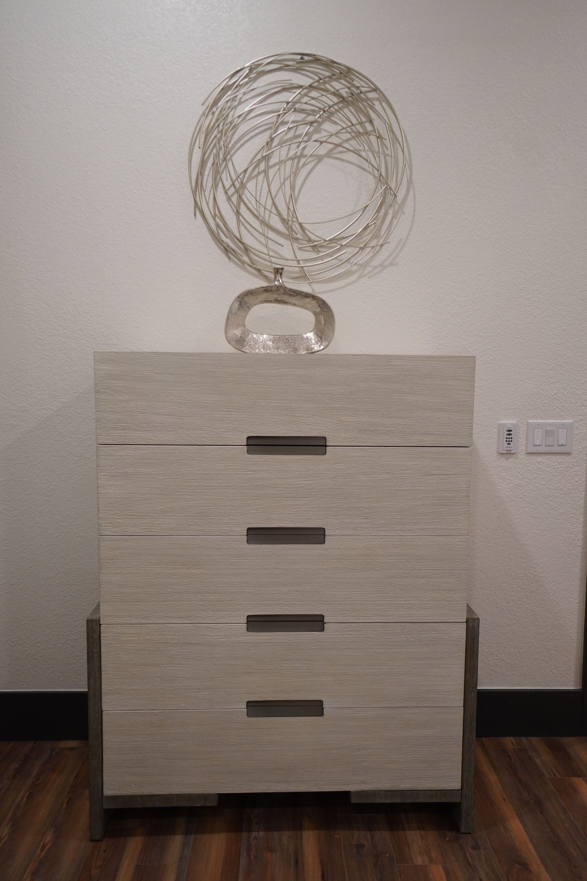 Chest of drawers with decorative wire sphere and glass ornament on top, set against a white wall.