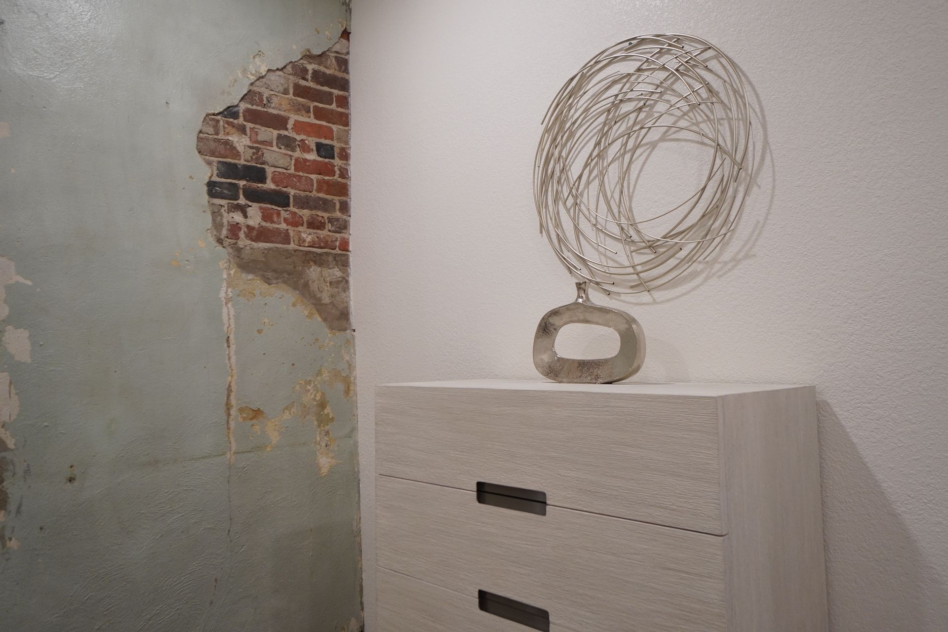 Sculpture on a white block against a wall with exposed brick and peeling paint.