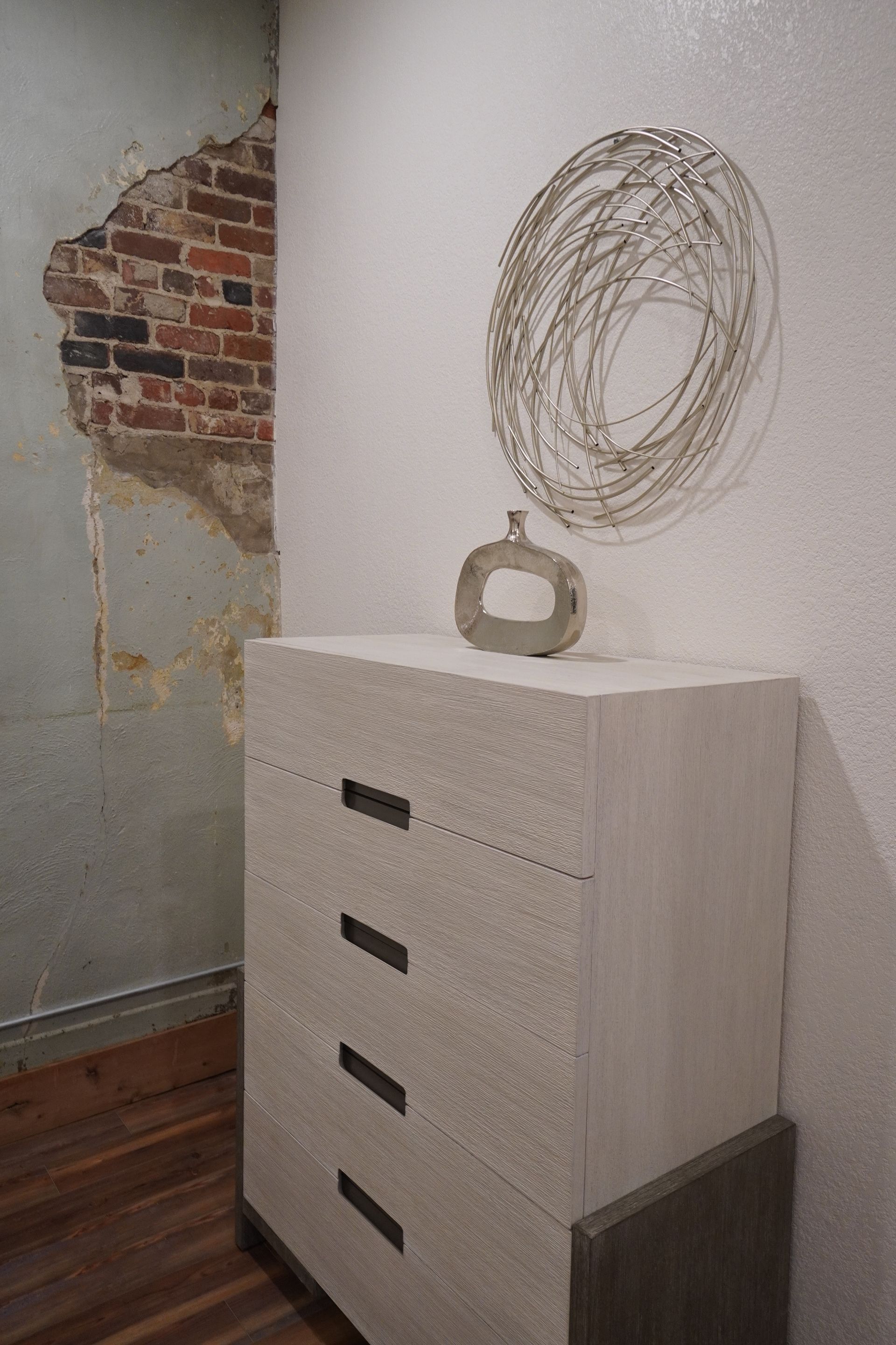 White dresser with decorative objects against white wall, exposed brick accent.