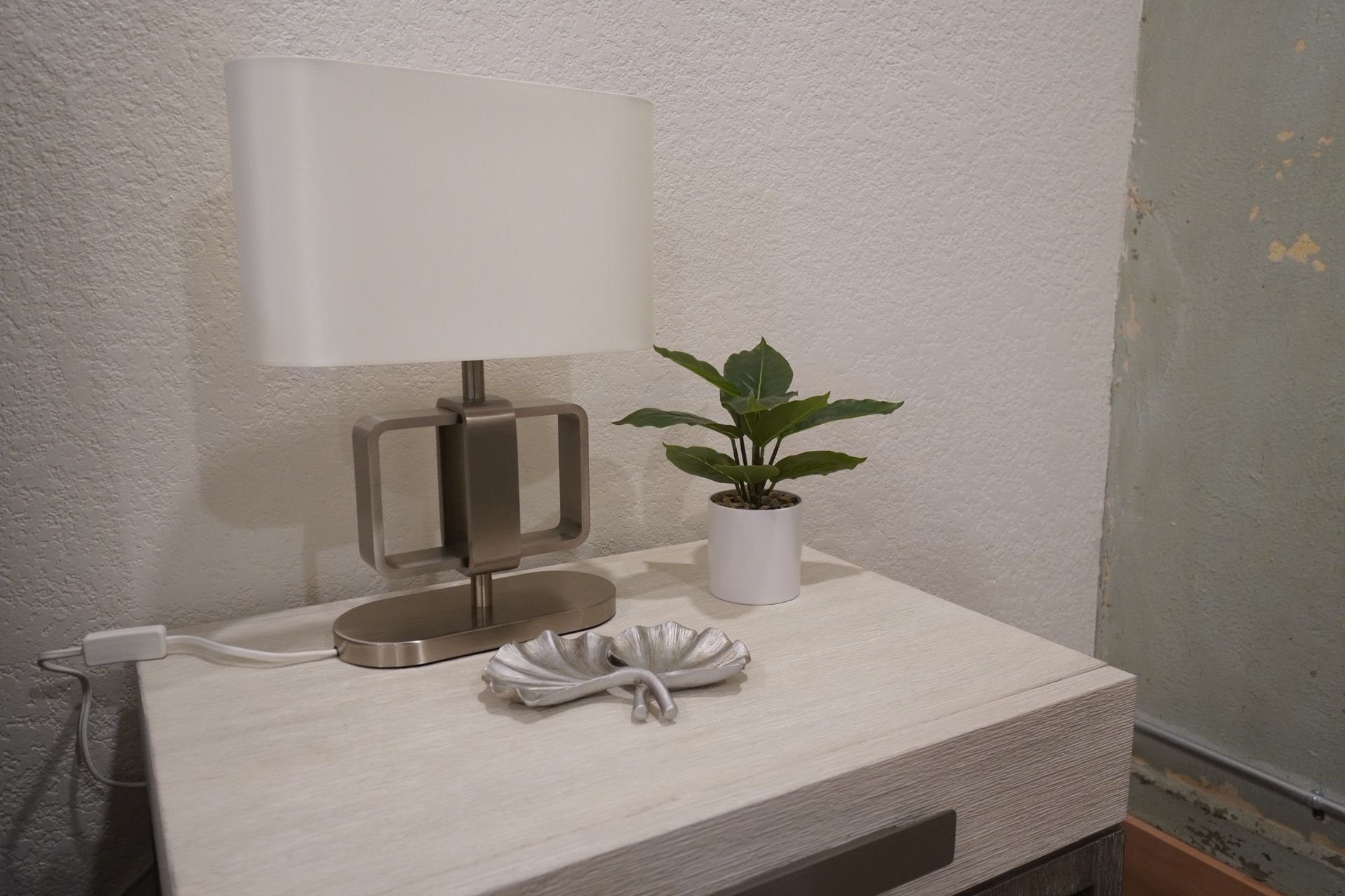 Nightstand with lamp, plant, and decorative dish against a white wall.