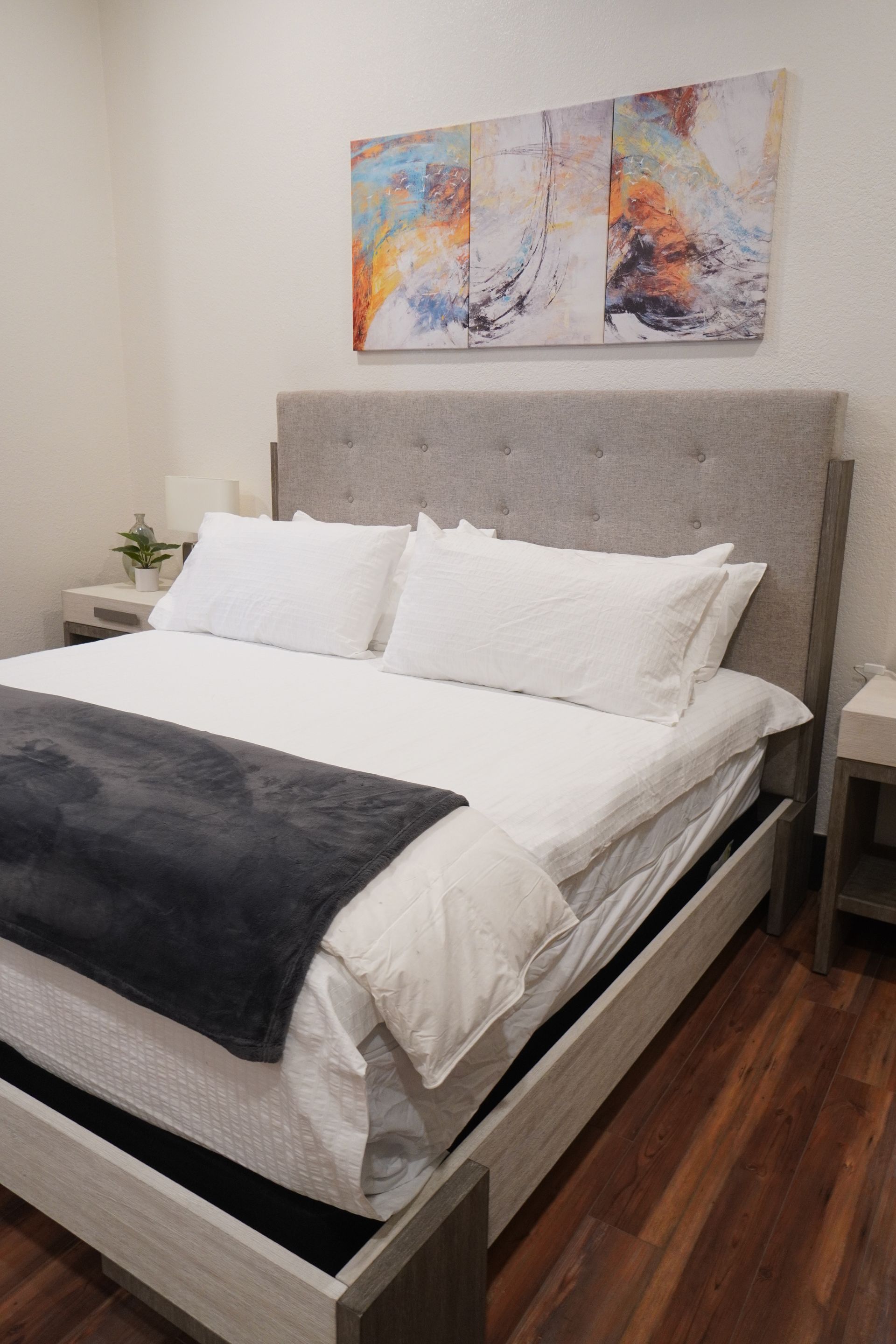 Bedroom with bed, nightstands, artwork, and hardwood floor.