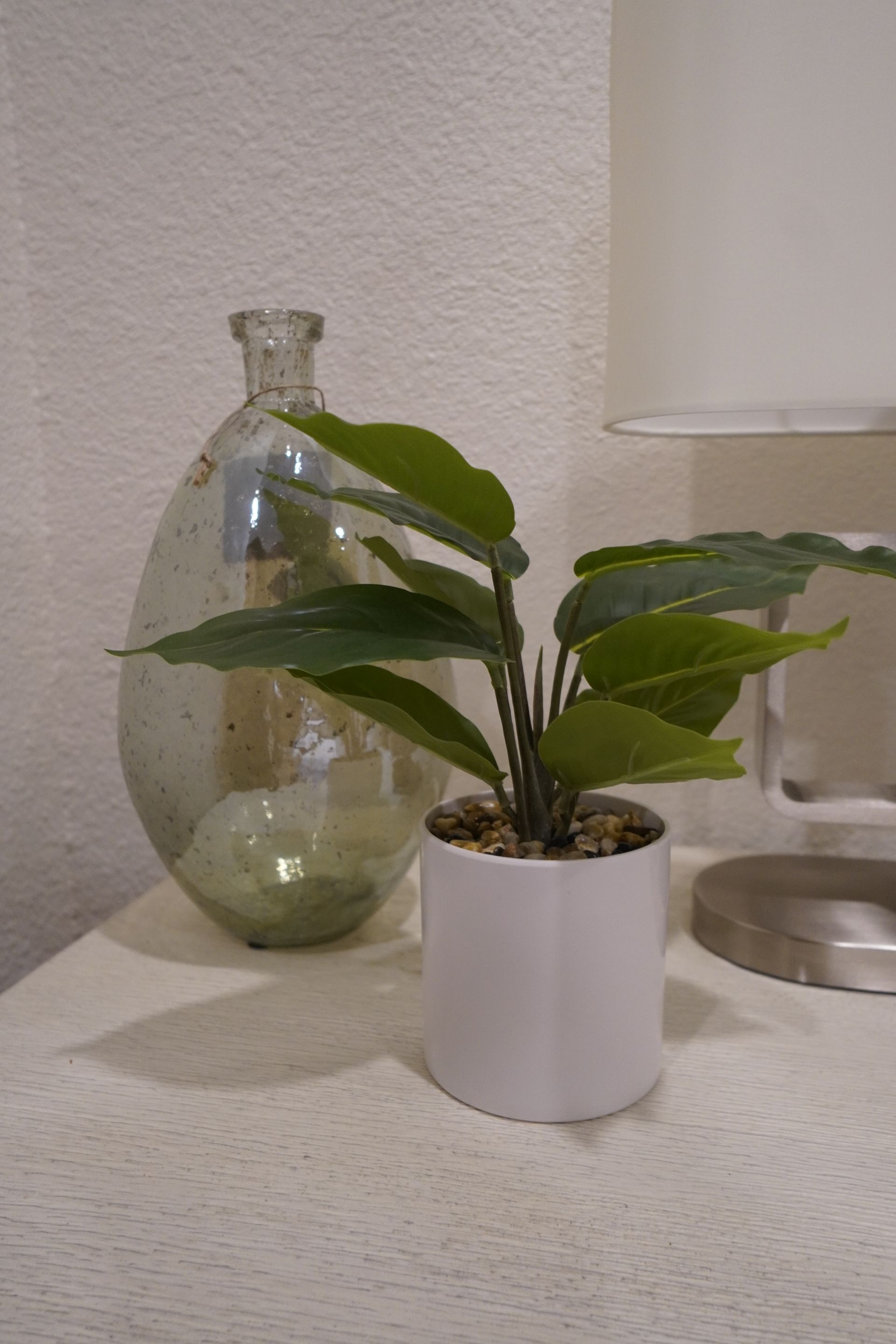 White pot with a small plant, silver vase, and lamp on a white table.