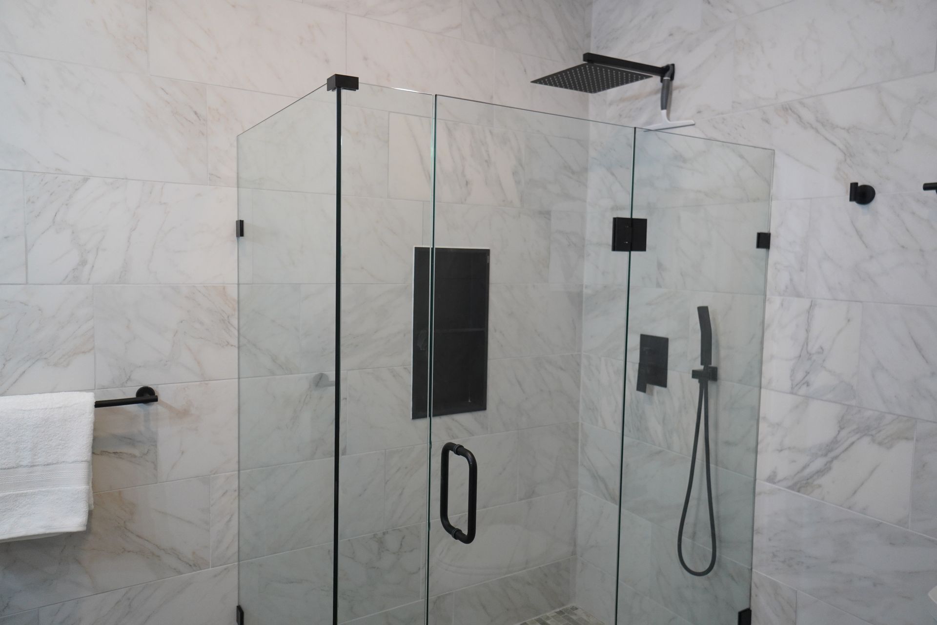 Glass shower enclosure with black fixtures and marble tile walls.