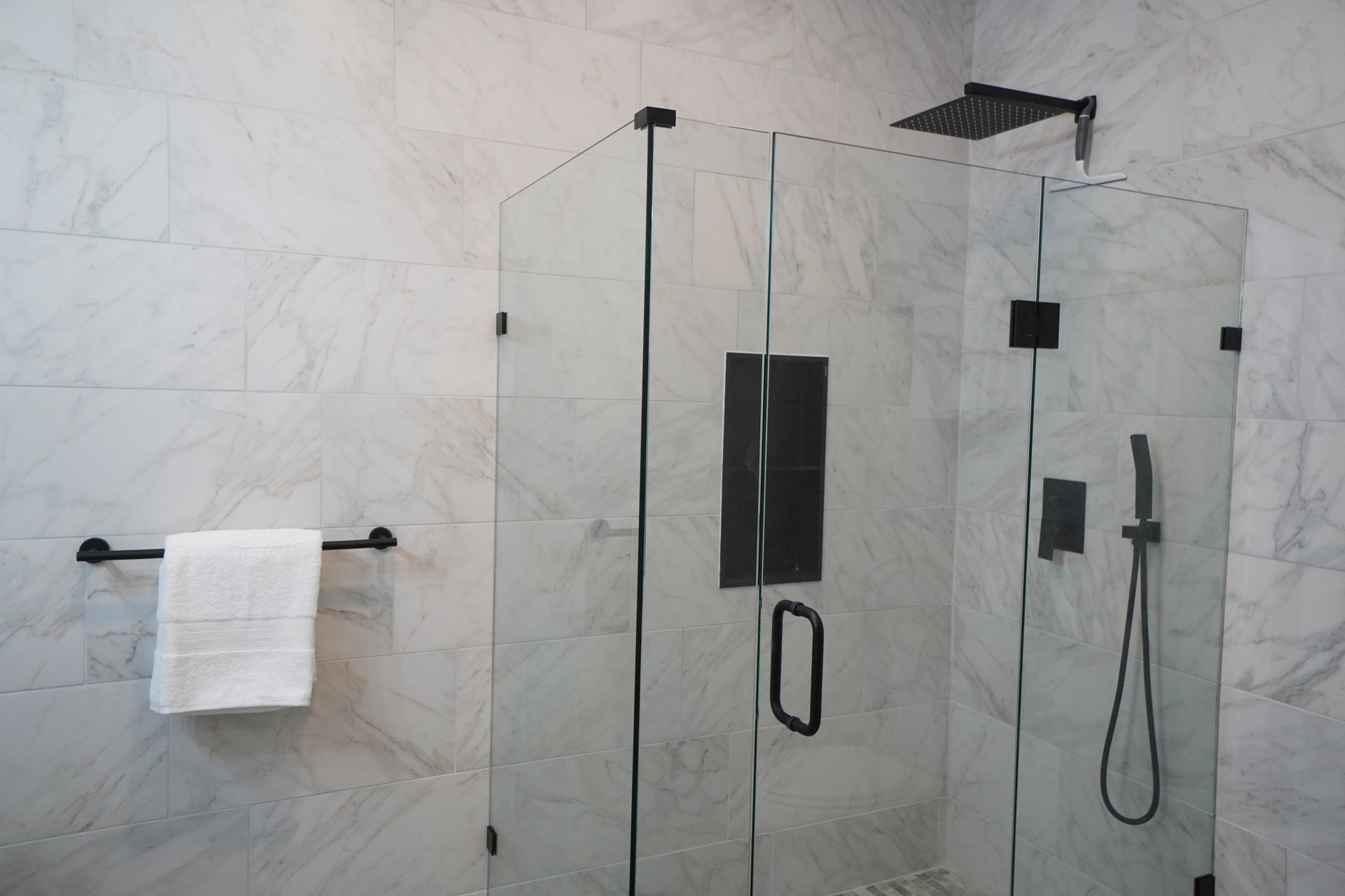 Modern bathroom with glass shower enclosure, black fixtures, and white marble tile.