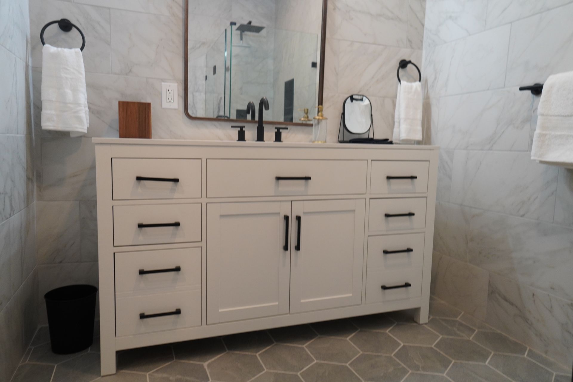 Bathroom with white vanity, black hardware, framed mirror, and gray tiled floor and walls.