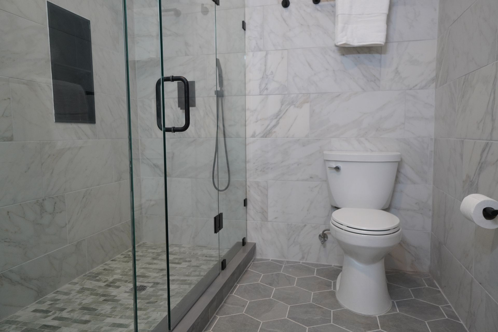 Bathroom with marble tile walls, glass shower, and gray honeycomb floor. White toilet.