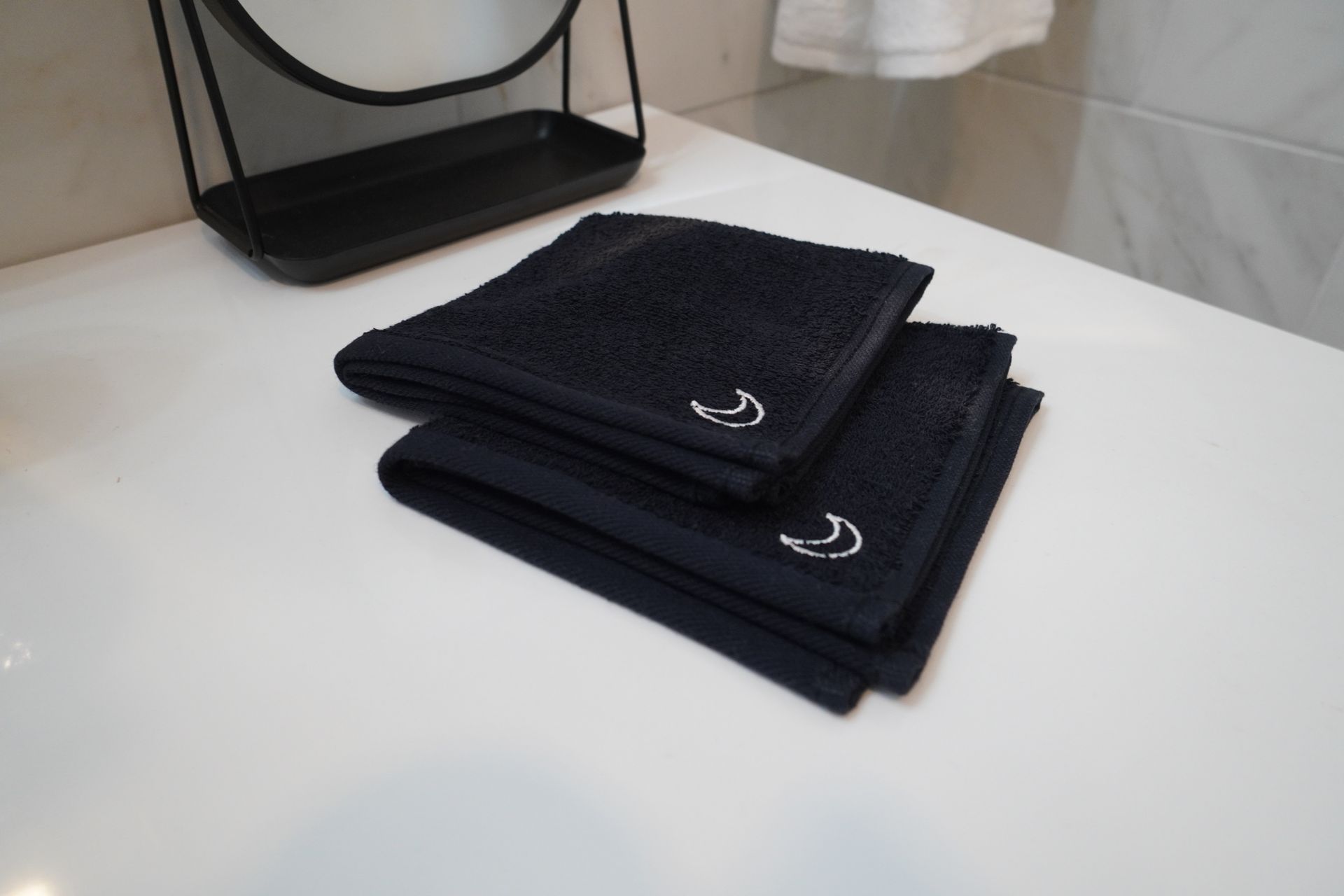 Two folded navy washcloths on a white counter; a black-framed mirror is in the background.