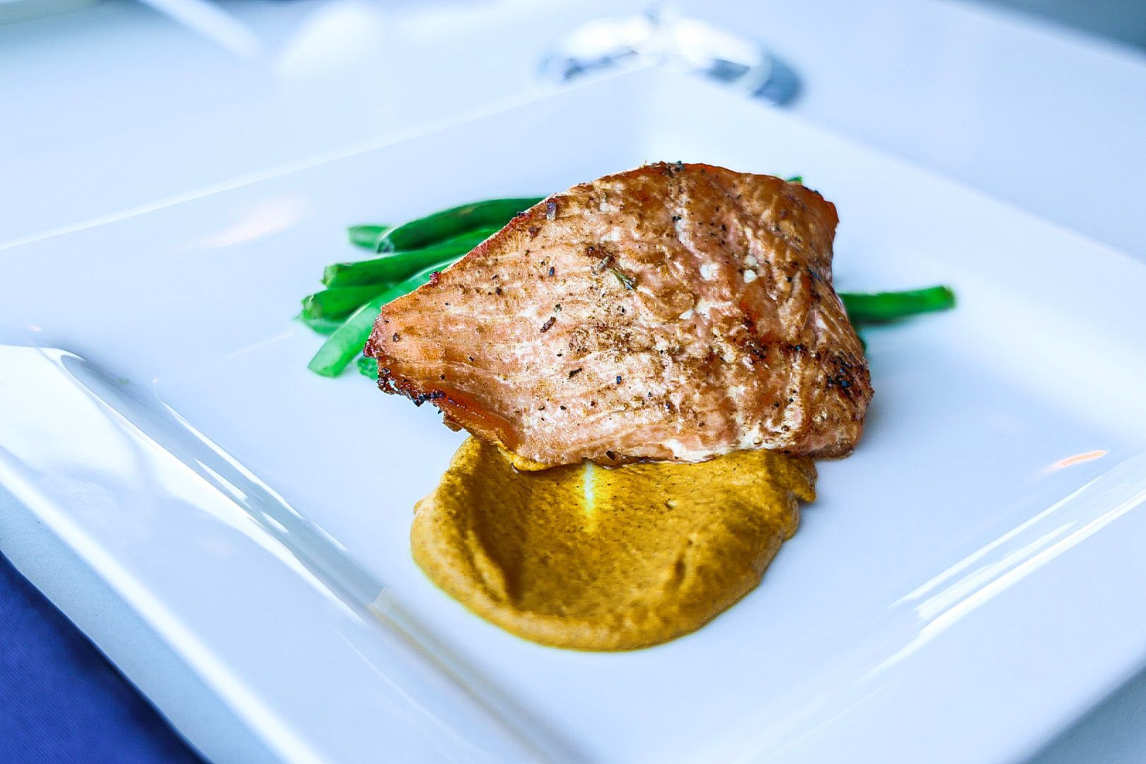 Salmon fillet with mustard sauce and green beans on a white plate.