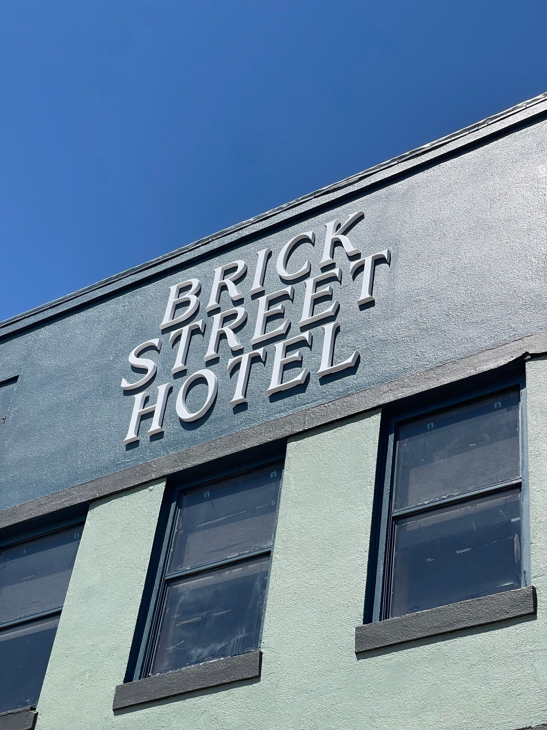 Brick Street Hotel sign on a teal building with dark-framed windows, against a blue sky.