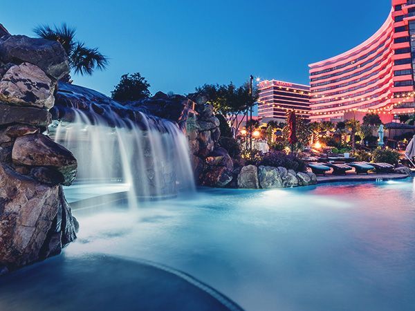 Pool with waterfall at dusk, resort buildings in the background.