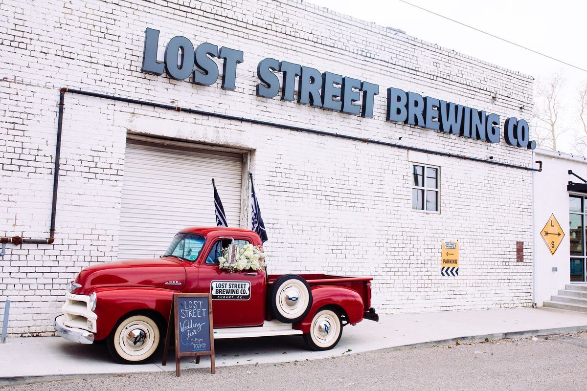 Red vintage truck parked outside Lost Street Brewing Co. building with white brick facade.